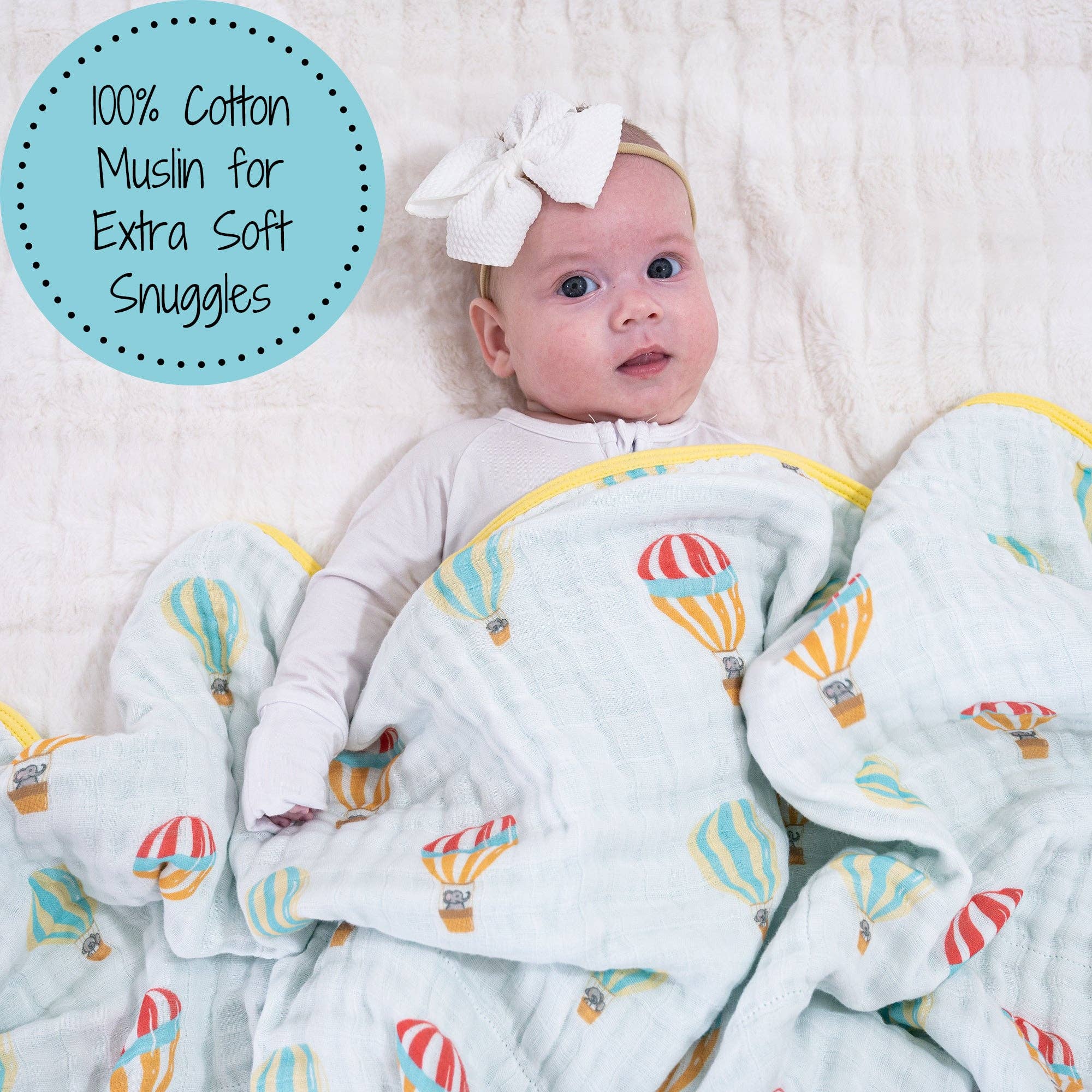 Baby wrapped in a blanket with hot air balloon pattern, wearing a white bow.