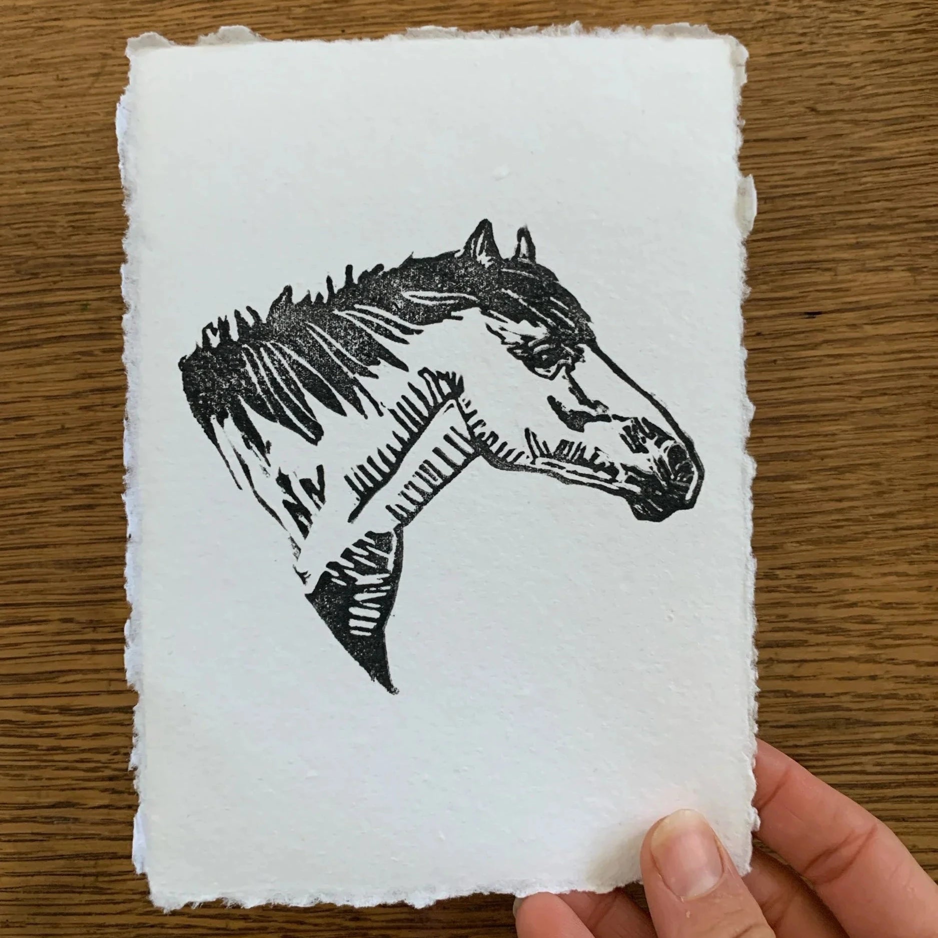 Rustic white paper with the bust ink transfer of a horse. Pictured in a person's hand against a wood back ground.