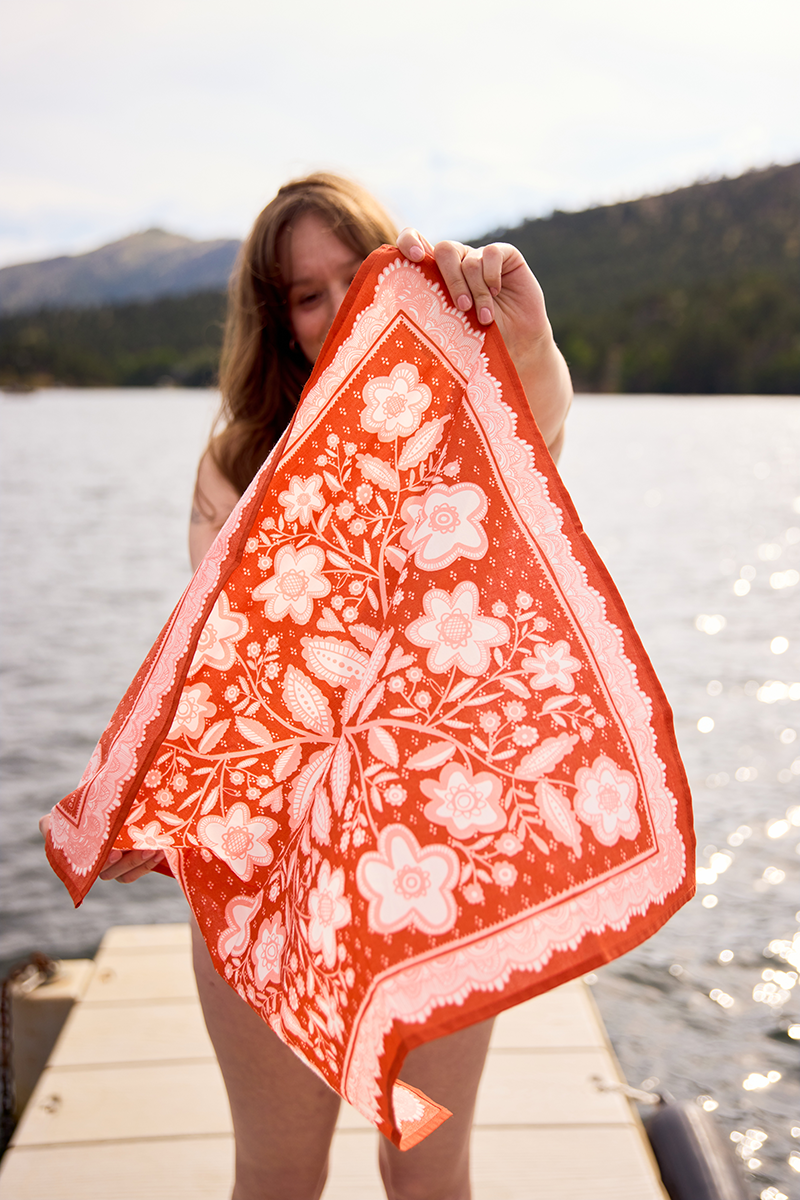 Person holding a red floral towel by a body of water with mountains in the background