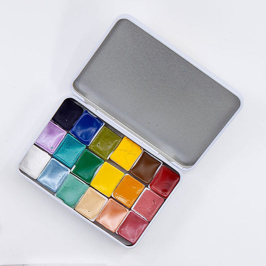 Mini paints in a range of colors set in a silver tin. Sitting atop a white back ground.