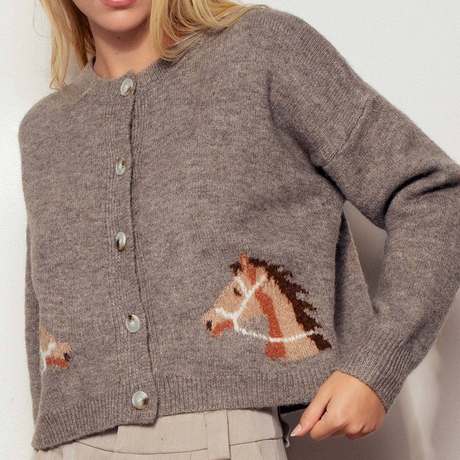 Mocha knitted cardigan with horse designs on a hanger against a light background