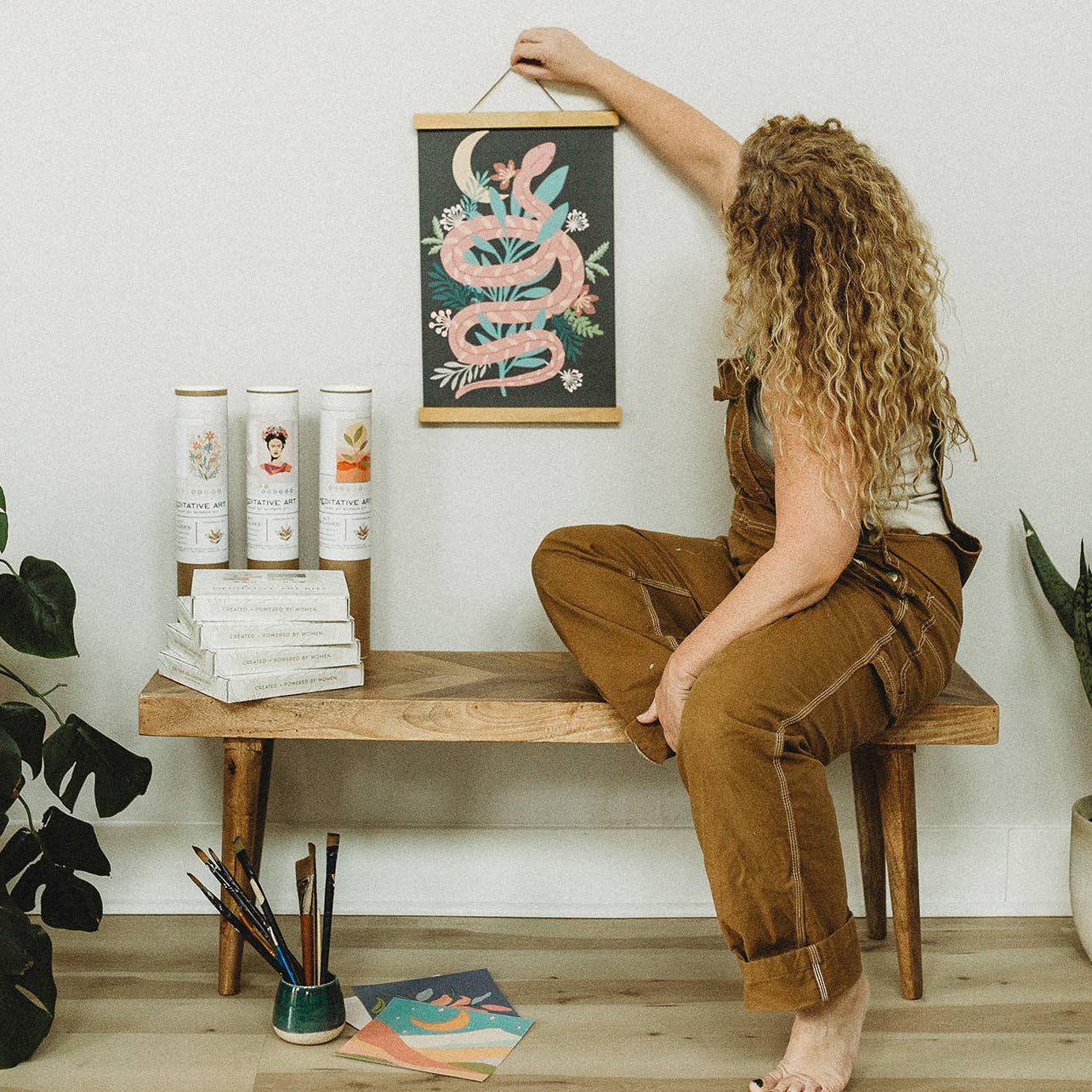 Woman sitting on a wooden bench with plants and books in a room.
