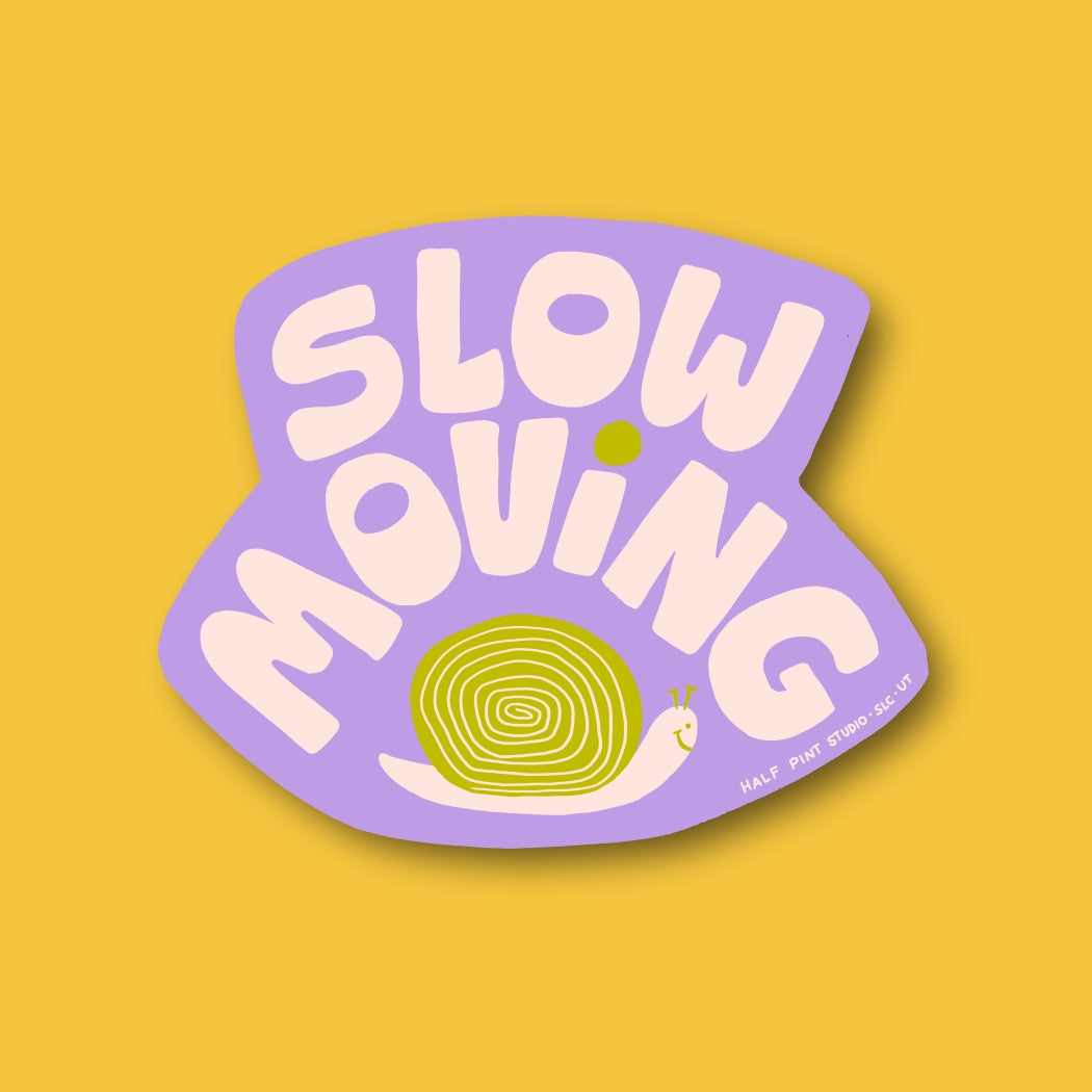 A playful vinyl sticker features the phrase “Slow Moving” in bold, rounded pink letters on a lavender background. Below the text is a cute green and white snail with a smiling face, creating a cheerful and whimsical design.