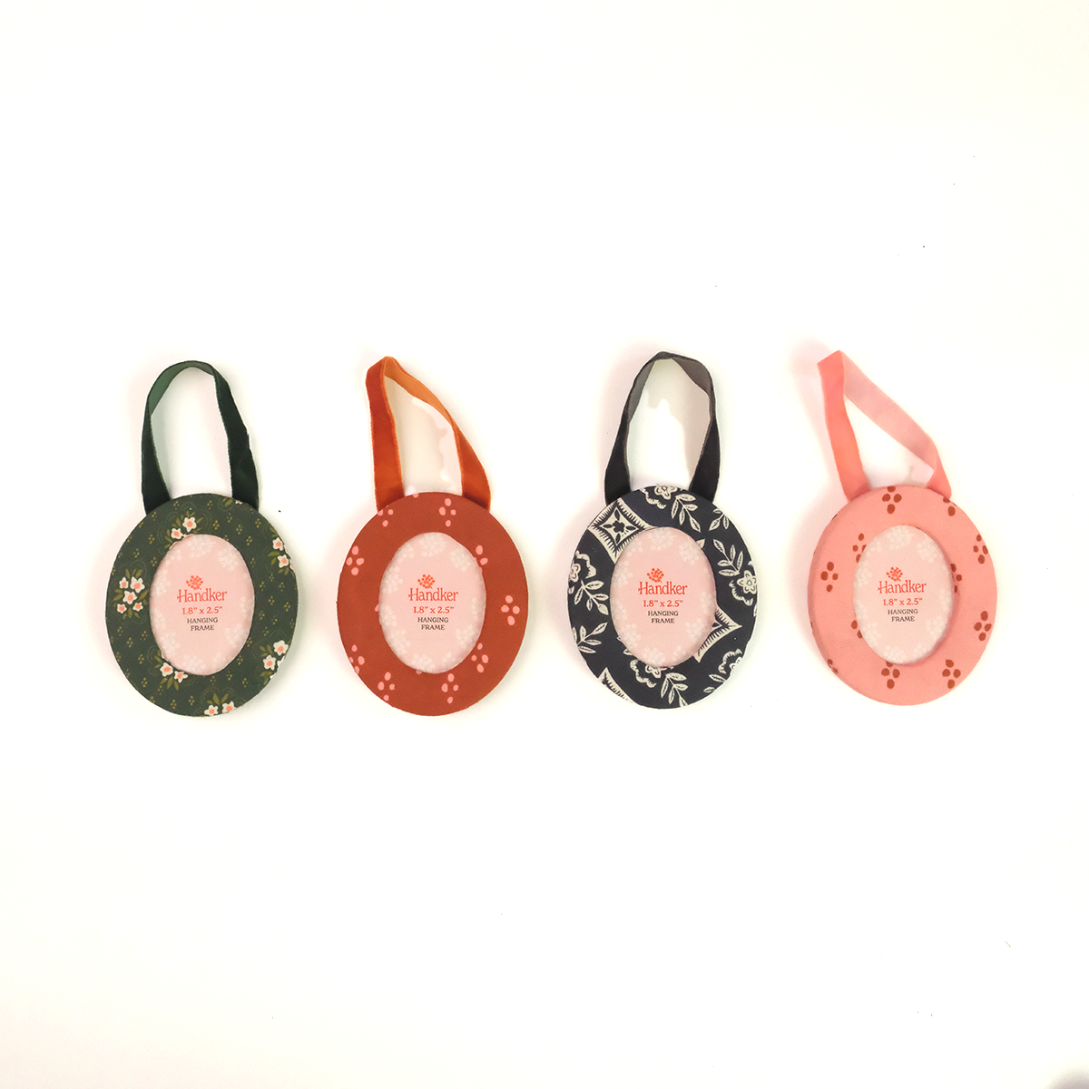 Four small fabric picture frames with hanging loops, arranged in a row on a white background. The frames are in different colors and patterns: dark green with white floral motifs, rust orange with small white floral motifs, black with white leafy patterns, and light pink with small red floral motifs.
