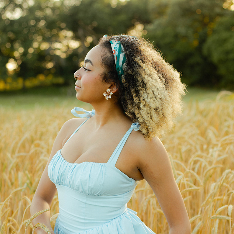Woman in a light blue dress holding a floral clutch in a wheat field