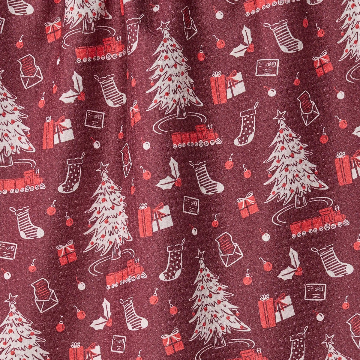 A close-up of a holiday-themed fabric print featuring Christmas trees, stockings, gifts, and trains on a dark burgundy background.
