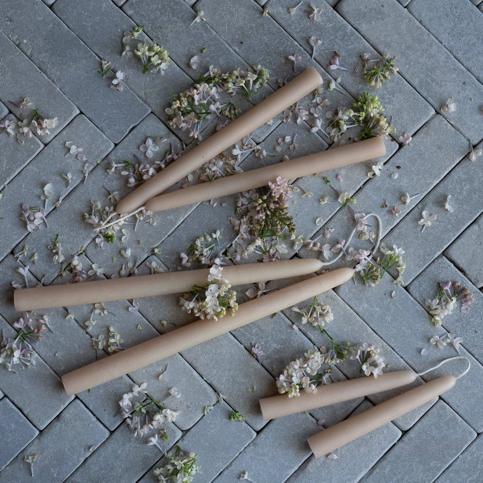 Four light color candles on a stone surface with scattered flowers