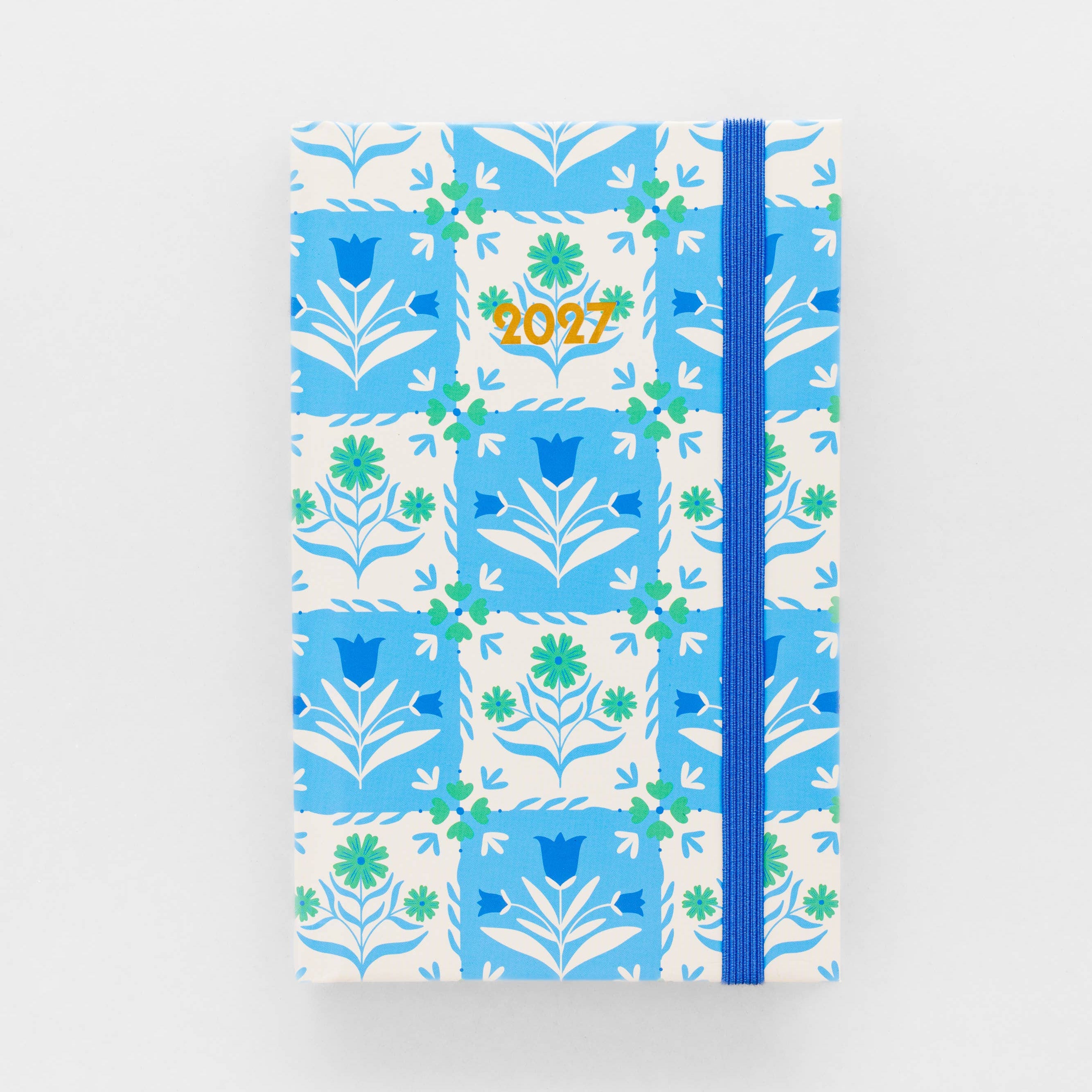A hardcover journal with a blue and white floral tile pattern, featuring a blue elastic closure band and a gold foil '2027' date on the cover, set against a plain white background.