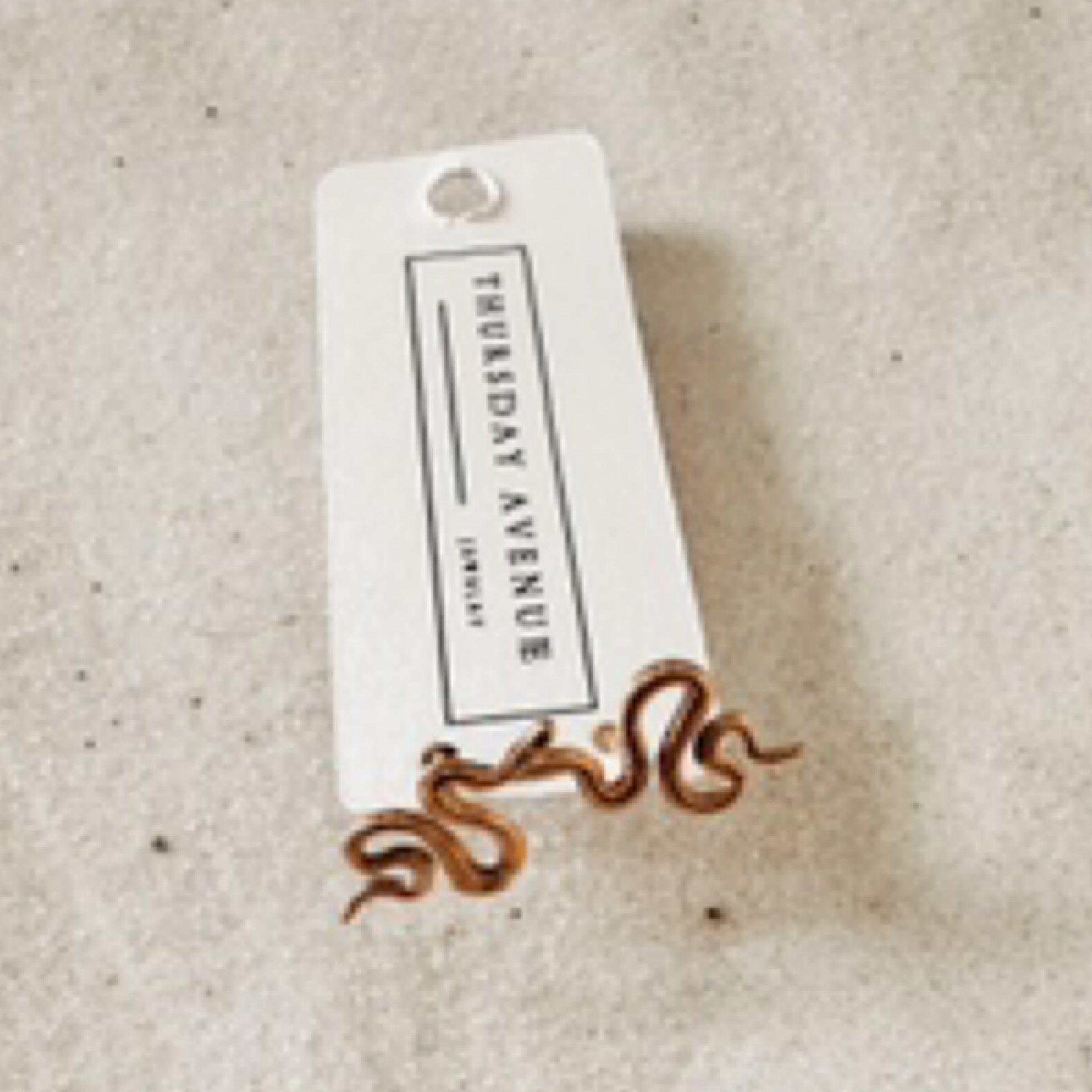 Gold snake flat back earrings. Pictured against white sand.
