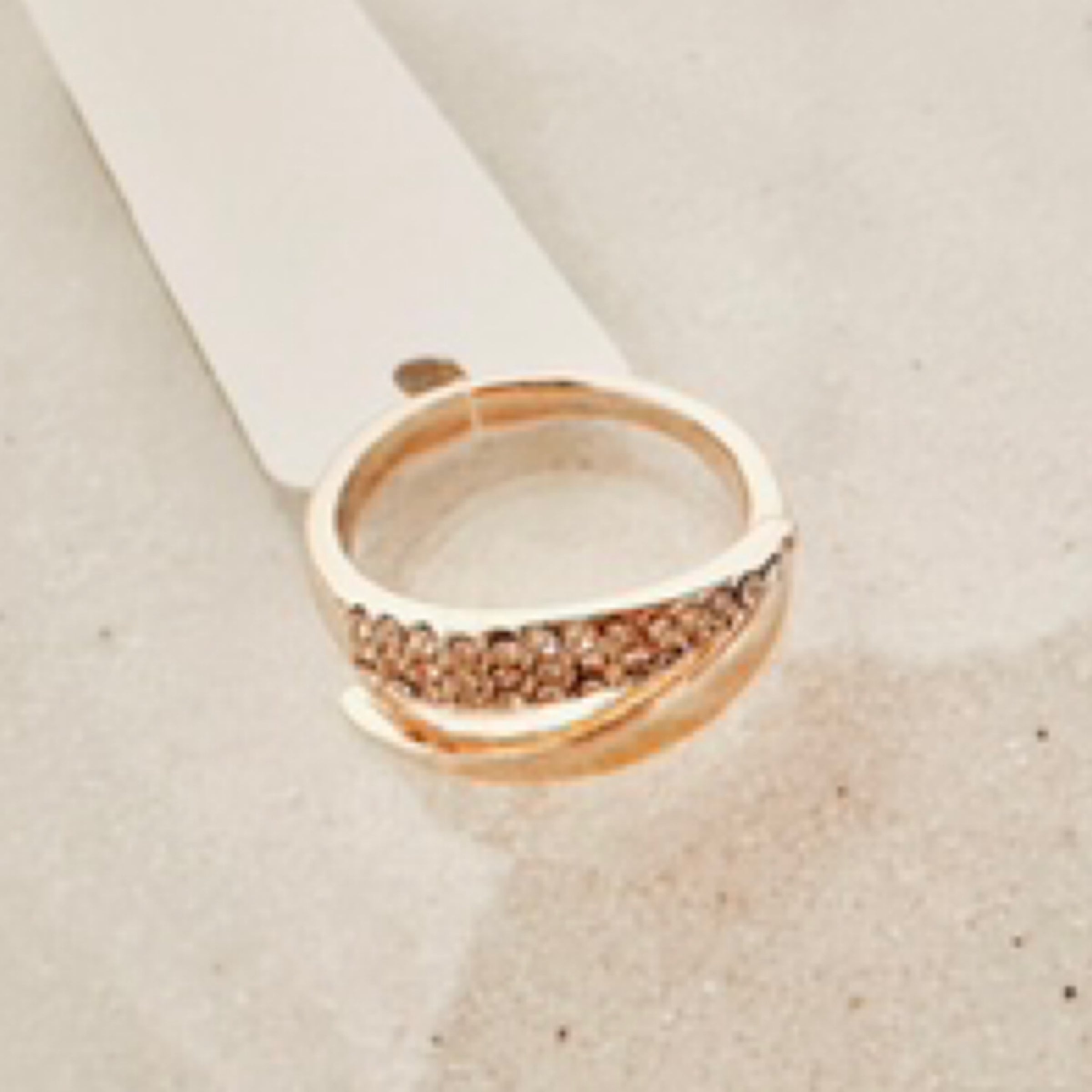 Gold adjustable ring that tappers into points across the top of ring. One end is sparkly, the other end is simple gold. Pictured against white sand.