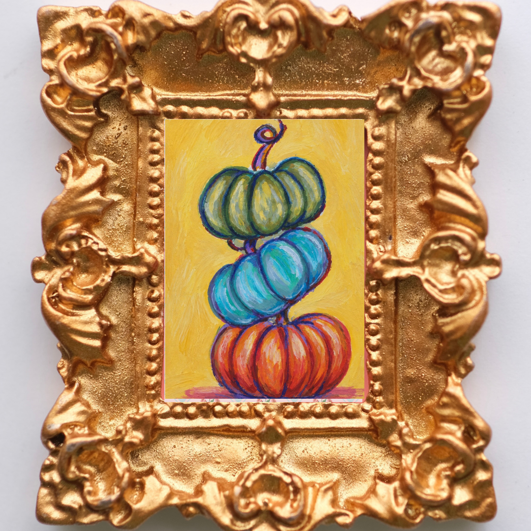 Trio of colorful pumpkins stacked in a tower. Inside a gold framed magnet.