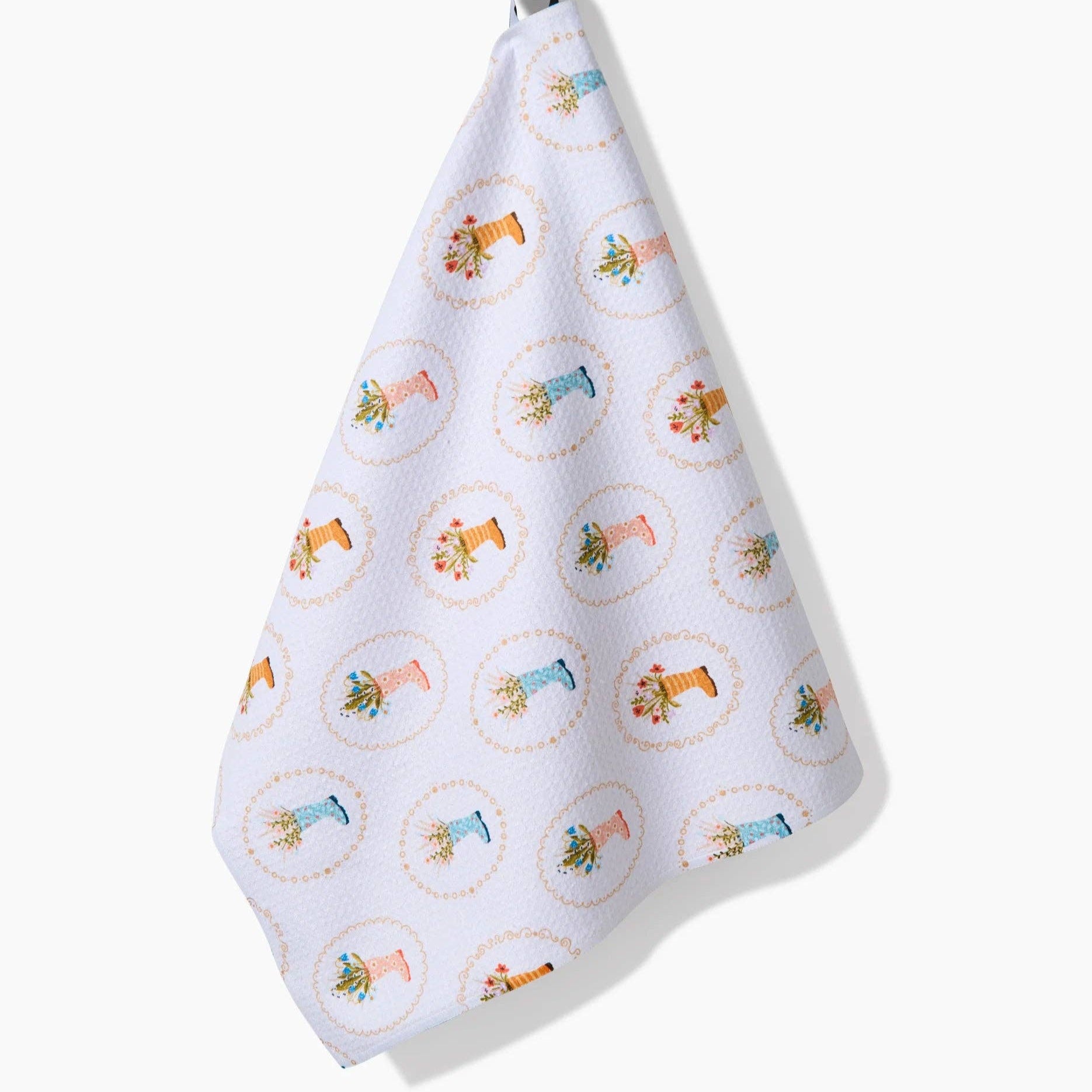 White towel with illustrations of rainboots holding flowers hanging on a white background