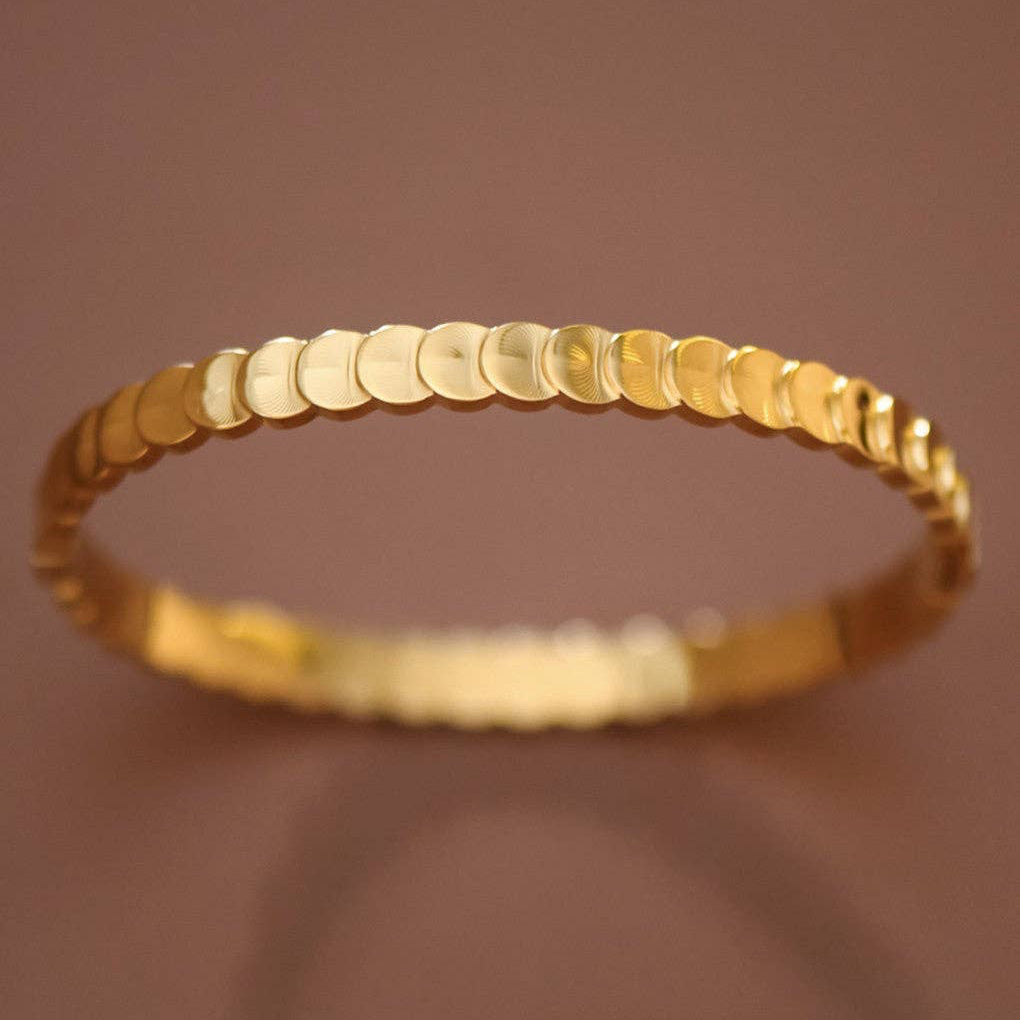 Elegant 18K gold plated stainless steel hinged bangle bracelet featuring delicate layered circles. With an inner oval diameter of 2.36" and 7" circumference, this piece offers a comfortable, versatile fit. Hypoallergenic, waterproof, and tarnish-resistant, it's designed to withstand daily wear and moisture exposure. The hinged closure makes it easy to slip on and off while maintaining a secure fit. To preserve the lustrous gold finish, avoid prolonged contact with lotions, perfumes, and harsh chemicals.