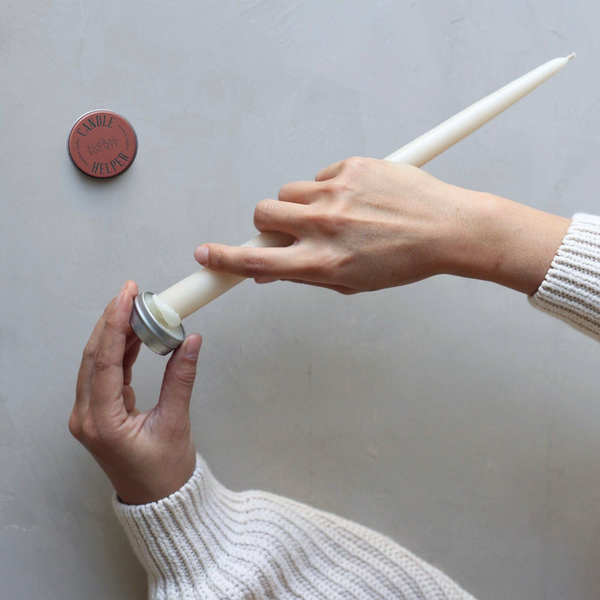 Person holding a candle with a small container of wax on a neutral background