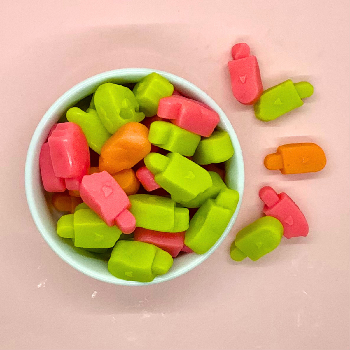 Green ,Pink and orange gummy popsicle shaped candy in a white bowl.