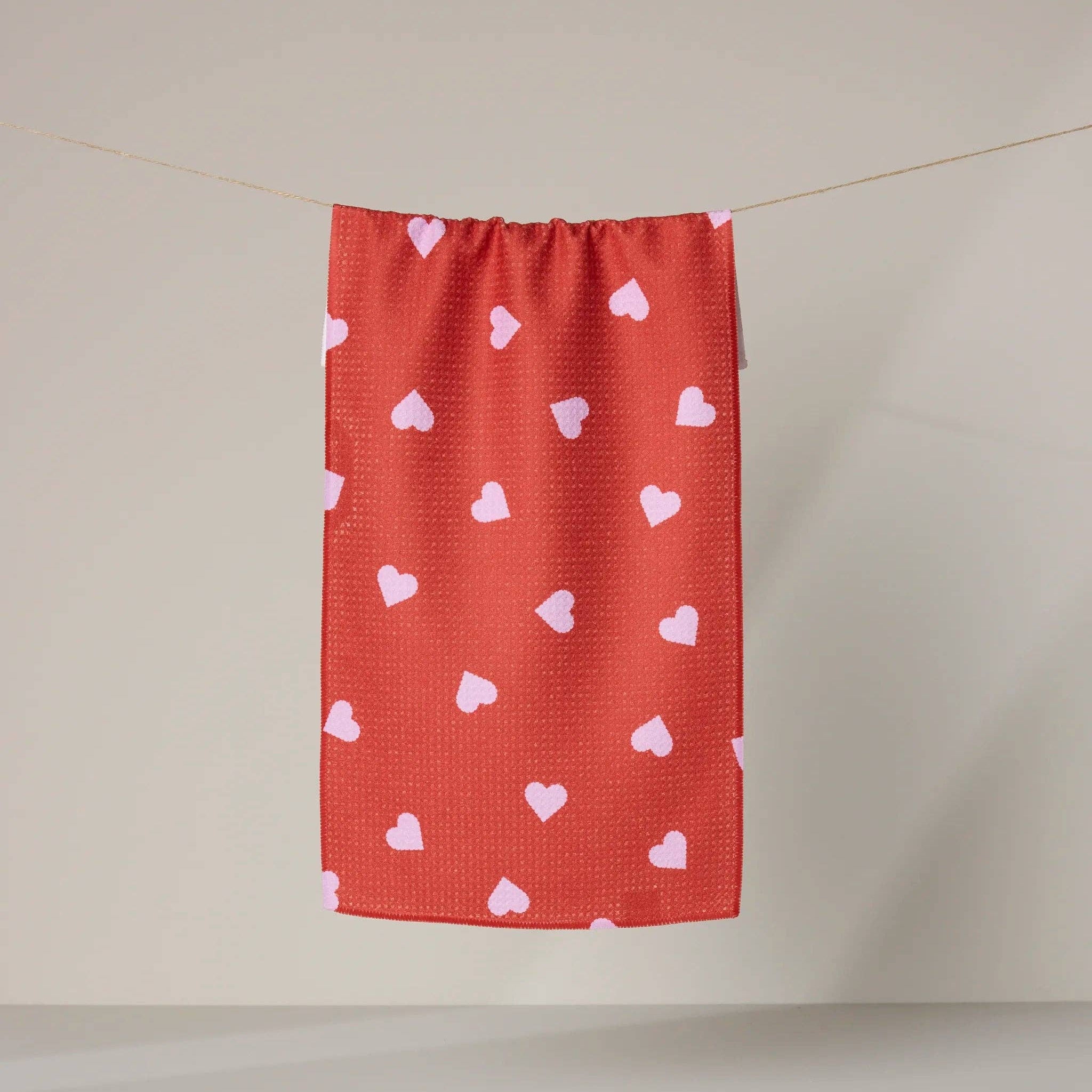 Red towel with pink hearts hanging on a line against a beige wall.