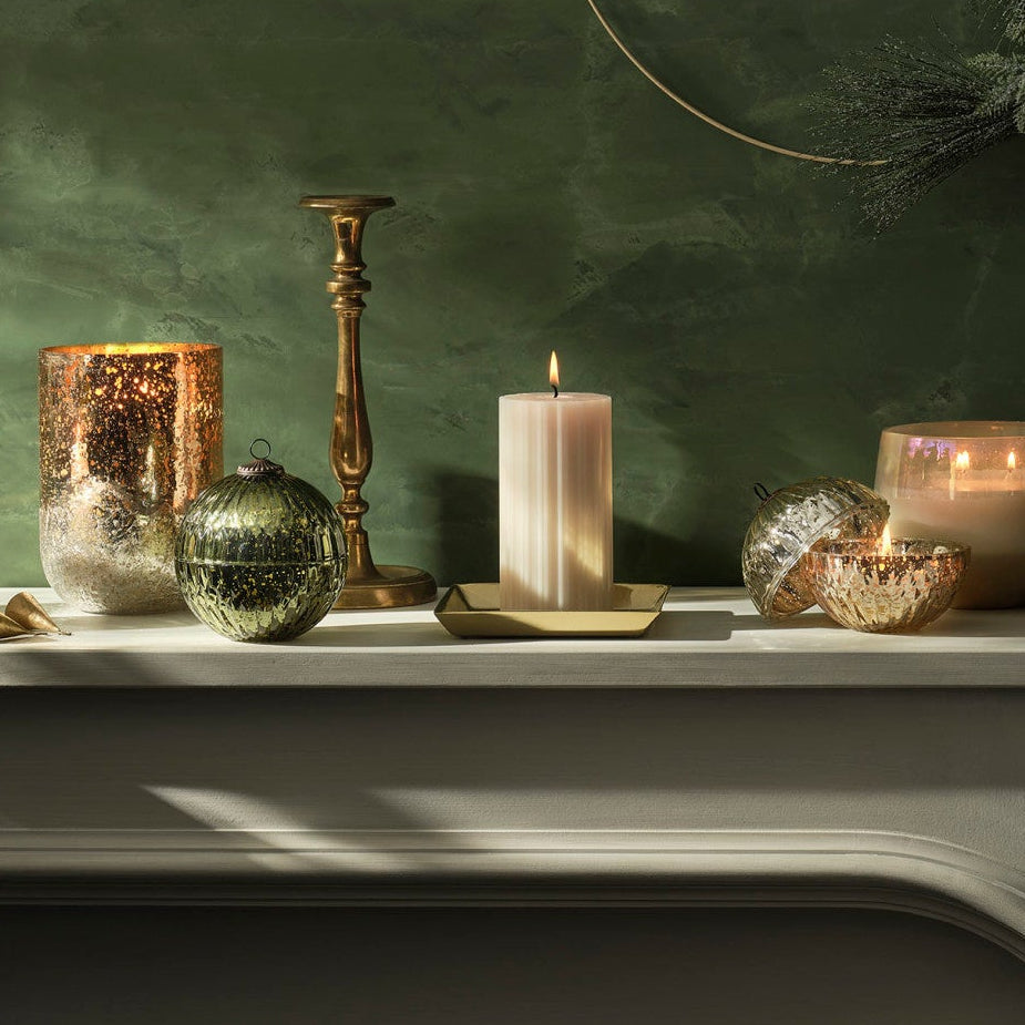Decorative mantelpiece with candles and glassware against a green wall.