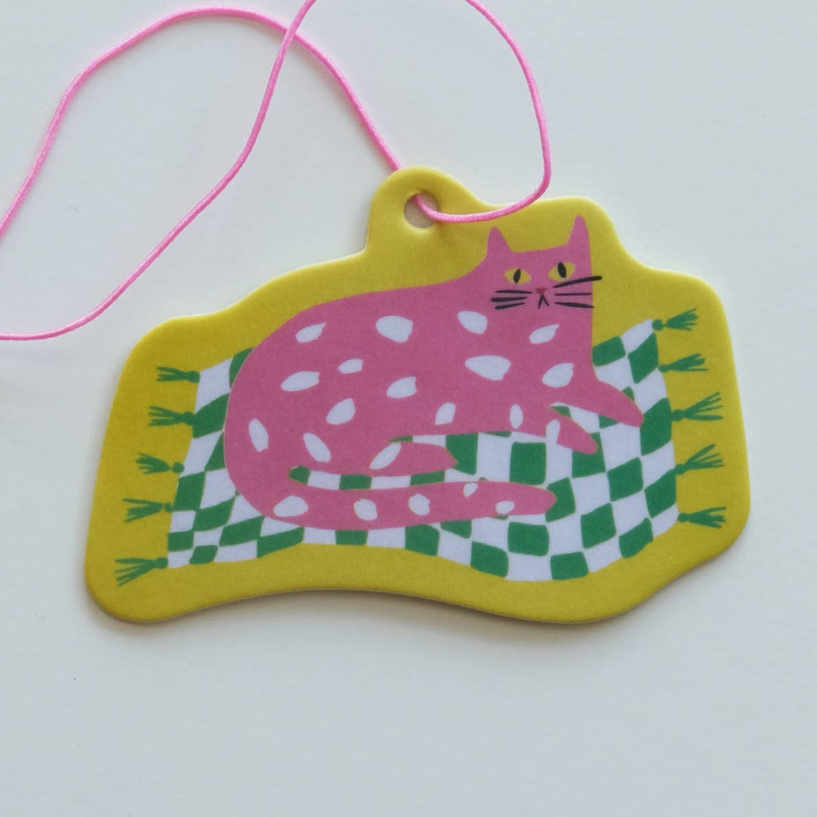 Colorful cat-shaped air freshener with a pink cat on a green and white checkered rug, attached to a pink string.