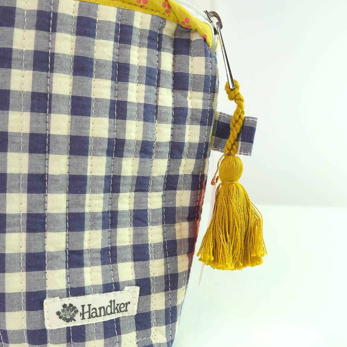 Blue and white checkered pouch with yellow tassel and 'Handler' brand label on a white background