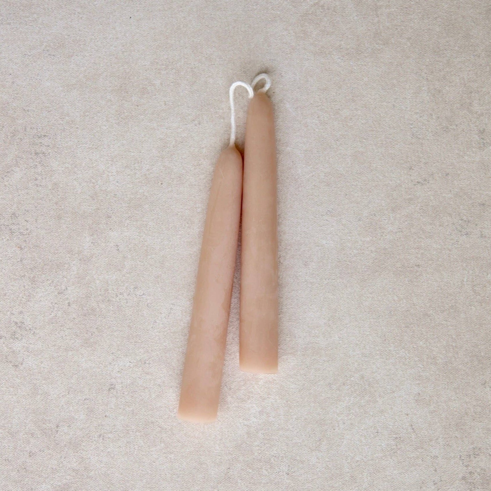 Two slim, tapered candles in a light rose color, arranged vertically side-by-side on a textured light gray surface.
