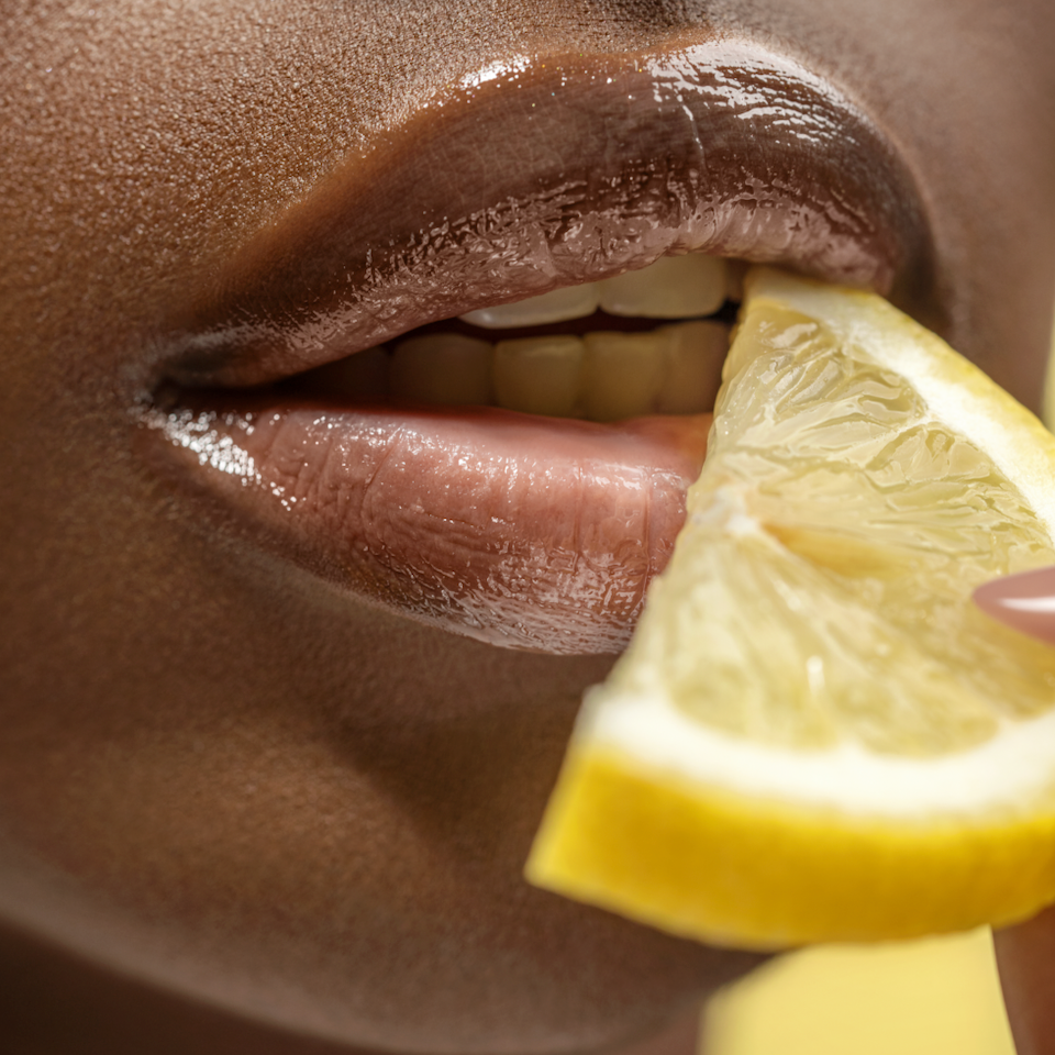 Close-up of a person holding a lemon wedge to their lips.