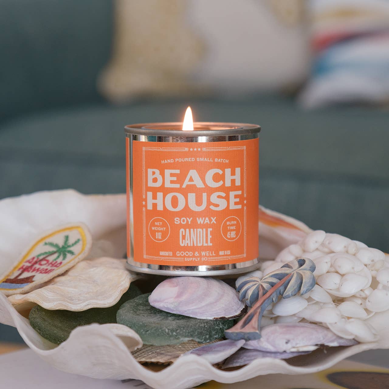 Beach House soy wax candle in a decorative container with seashells and sand.