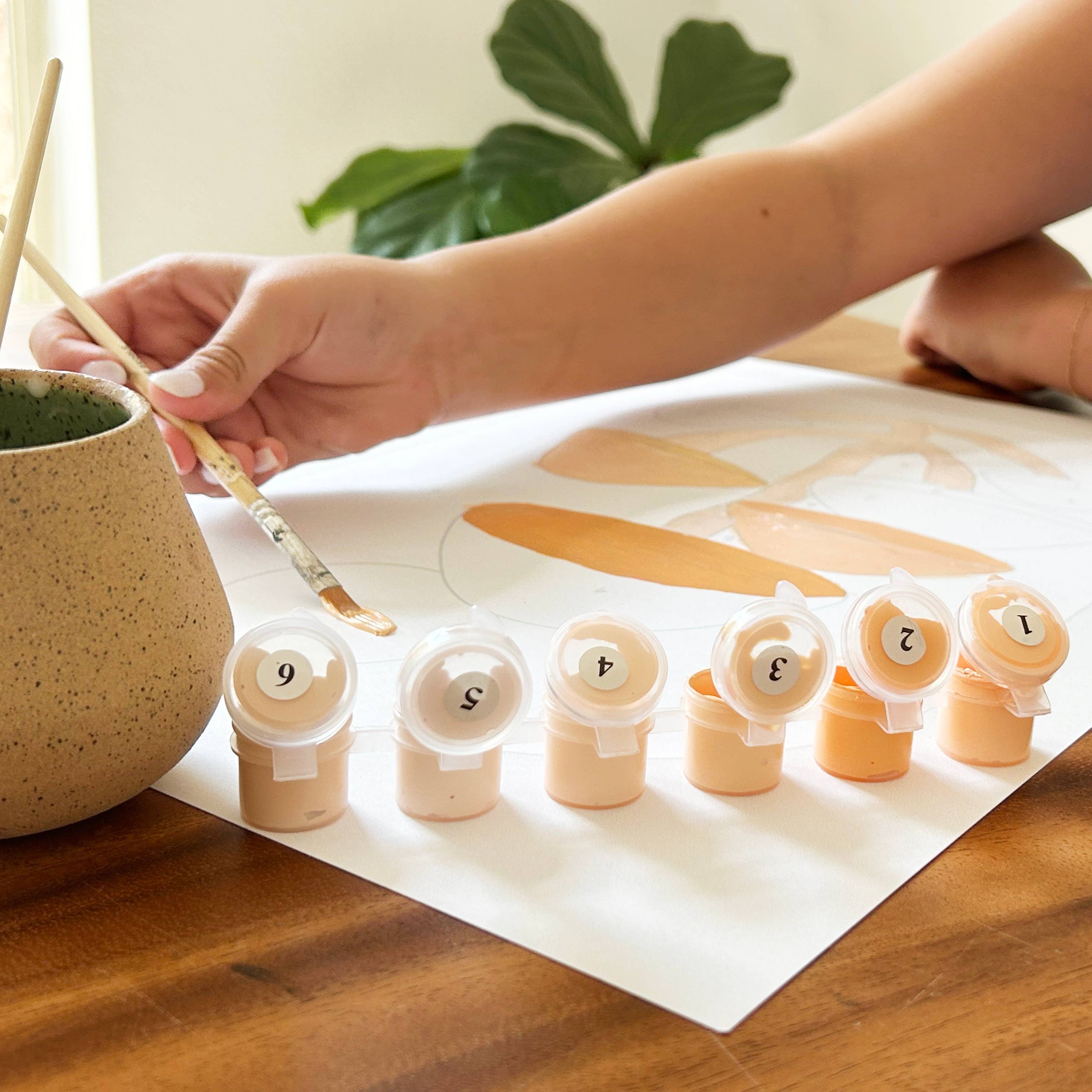 Person painting wooden numbers with a brush on a wooden table.