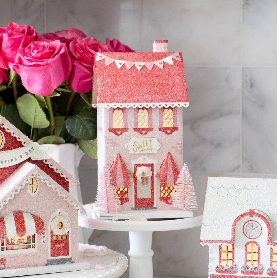 Welcome to the sweetest spot in your Valentine village! This charming Sweets Shoppe brings festive fun to your holiday display with its whimsical design and cheerful details. Perfect for creating a magical miniature world, this paper house adds character and warmth to any Valentine-themed village setup. Whether you're building an elaborate display or adding a special touch to your mantel, the Sweets Shoppe is your ticket to spreading joy and creating unforgettable holiday memories!