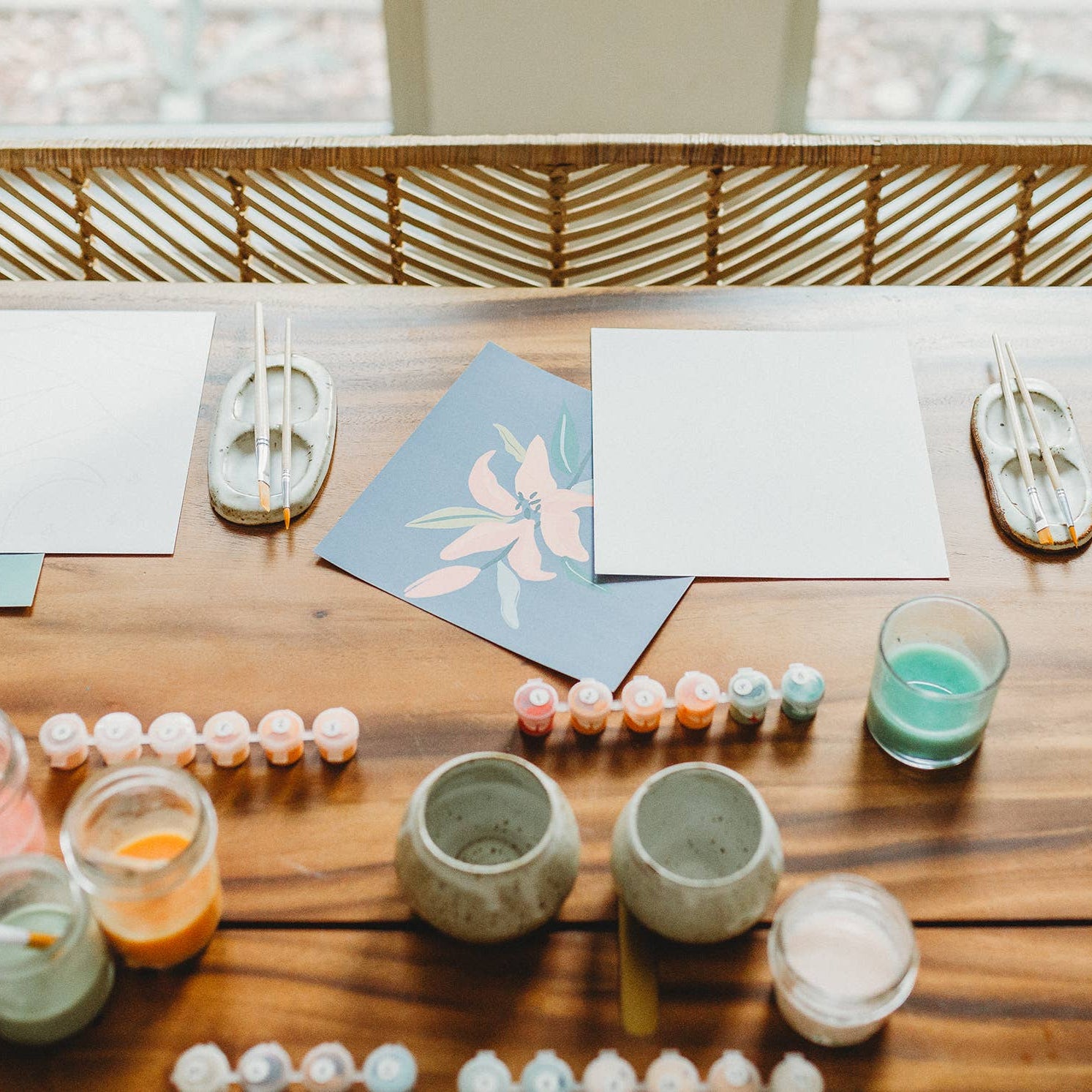 Table with ceramic cups, paint containers, and art supplies on a wooden surface.