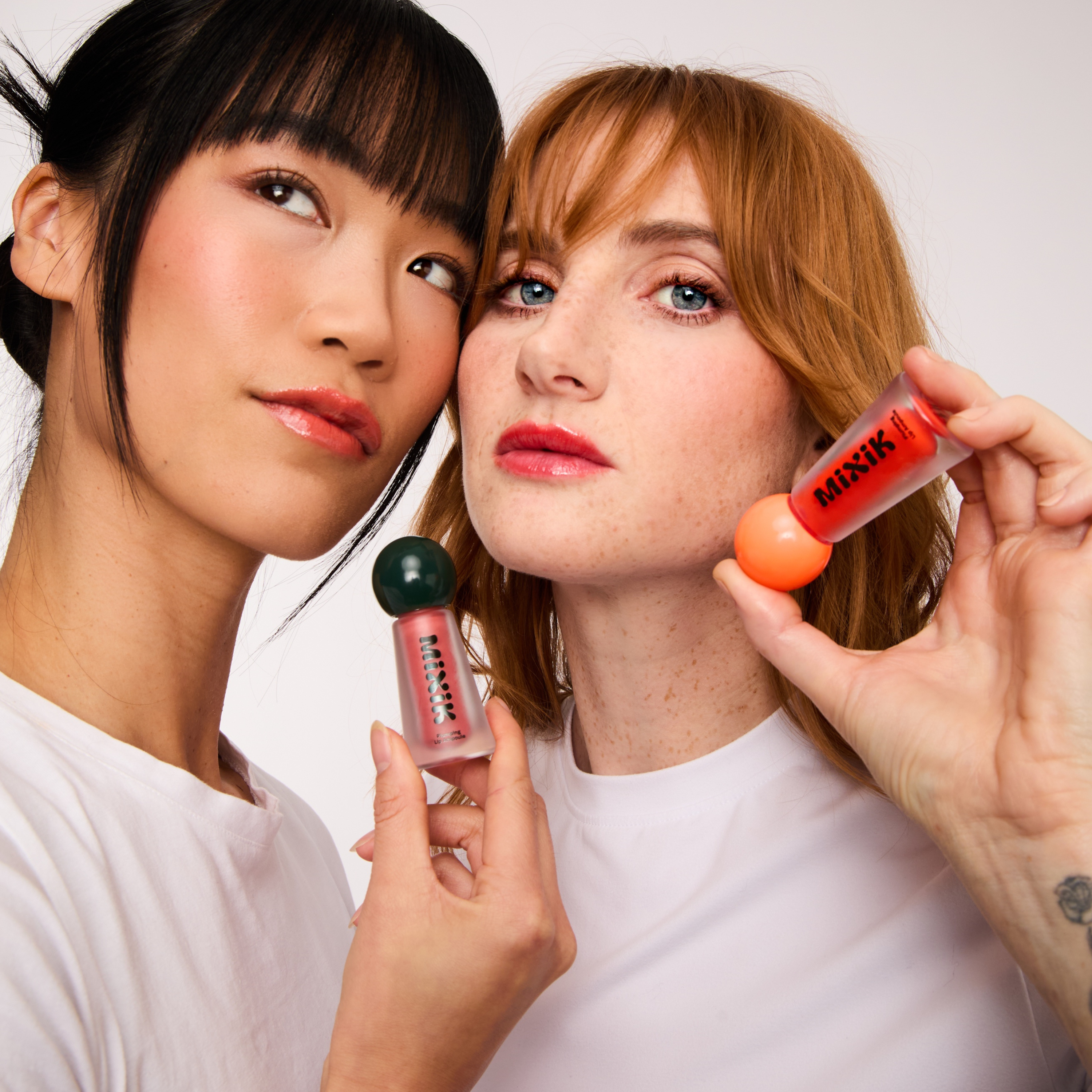 Two women holding makeup products against a white background