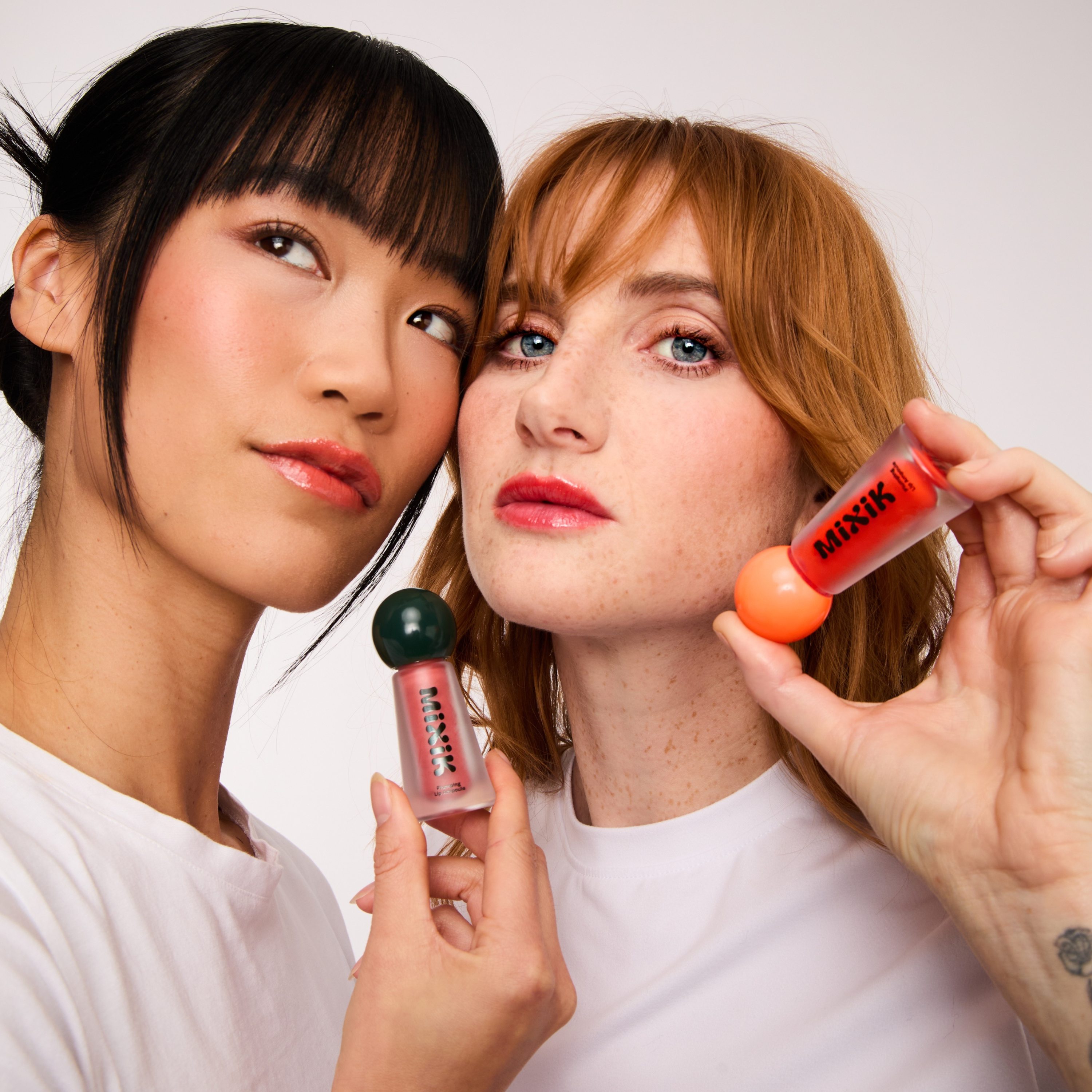 Two women holding makeup products against a white background