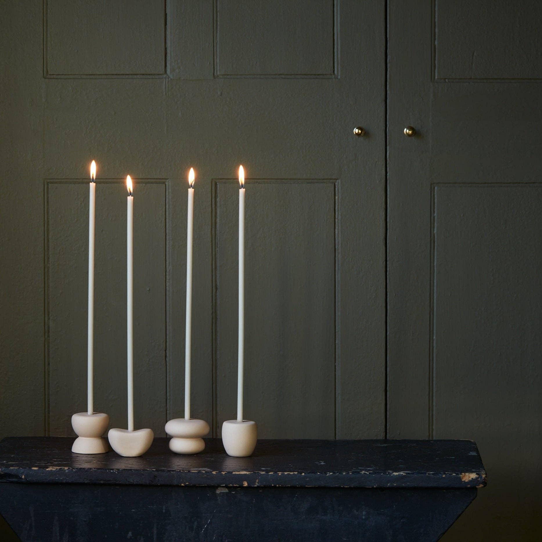 Four lit candles in stone holders on a dark surface against a green paneled wall.