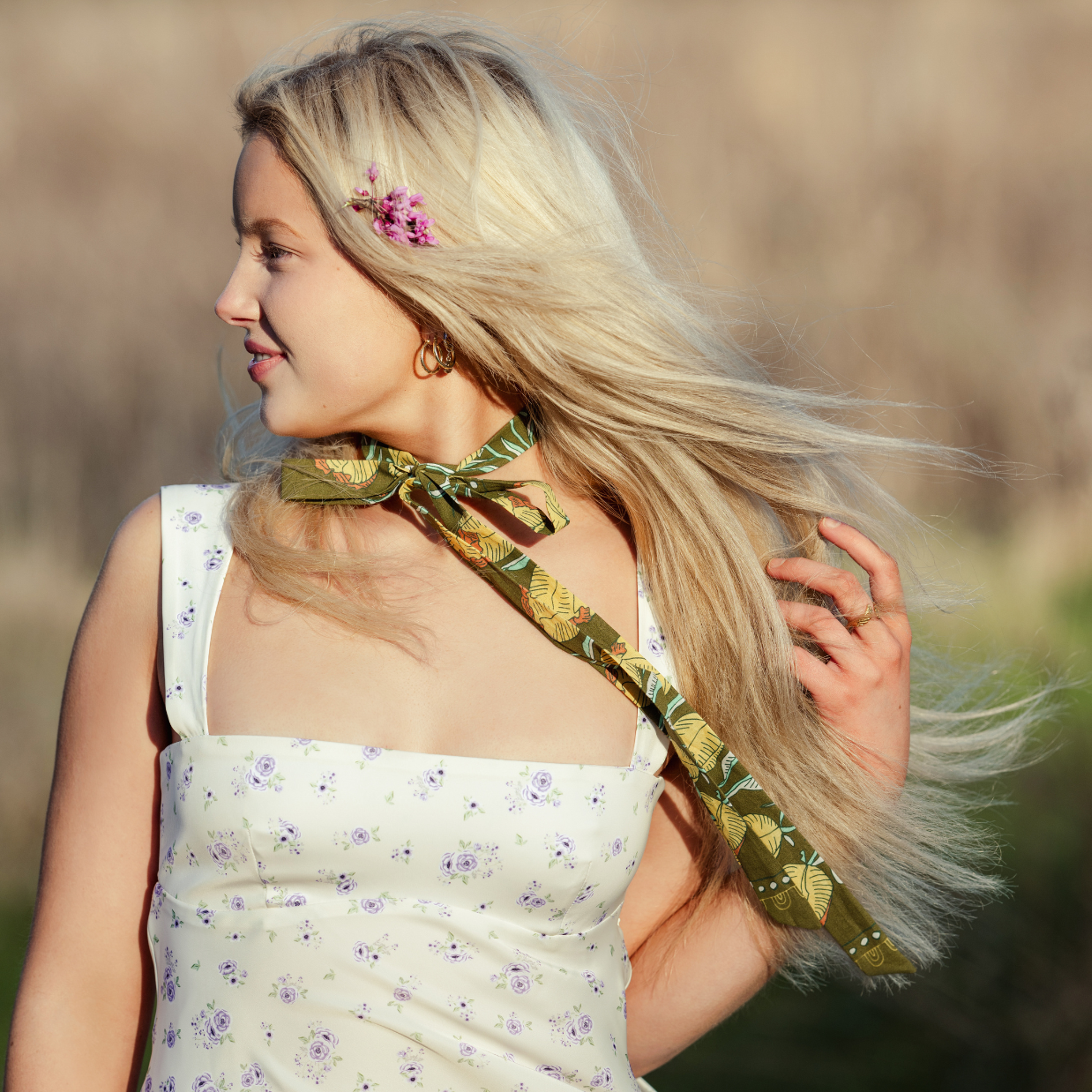 Woman with long blonde hair wearing a floral dress and green scarf in a natural setting