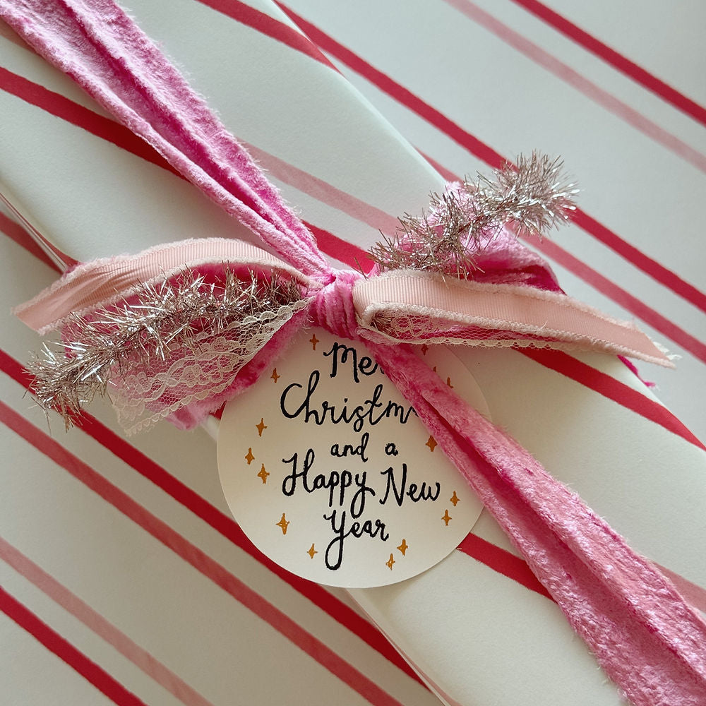 Candy cane stripe wrapping paper with a raw fabric pink bow with tinsel and tag.