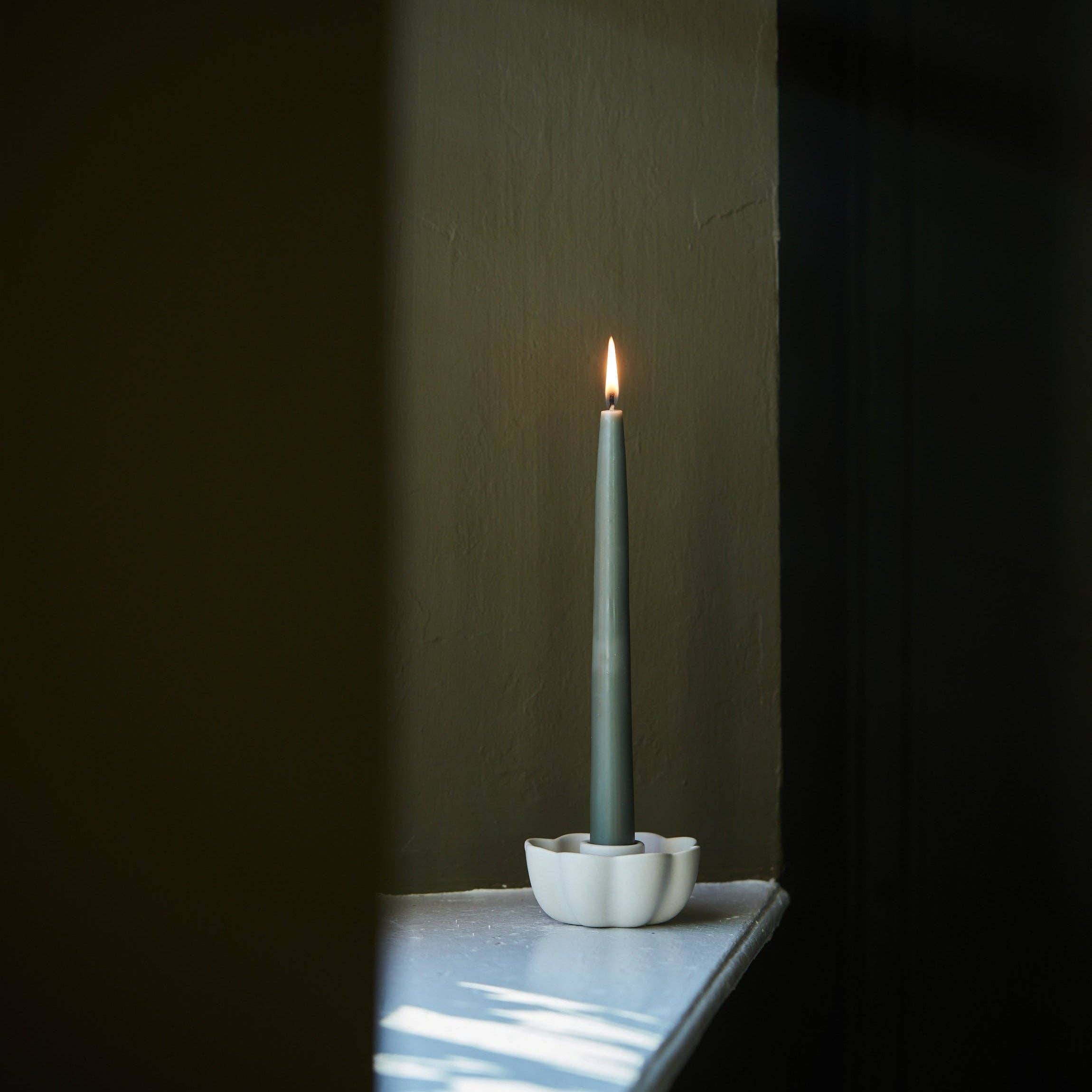Green candle in a white holder on a dark surface with a dark background