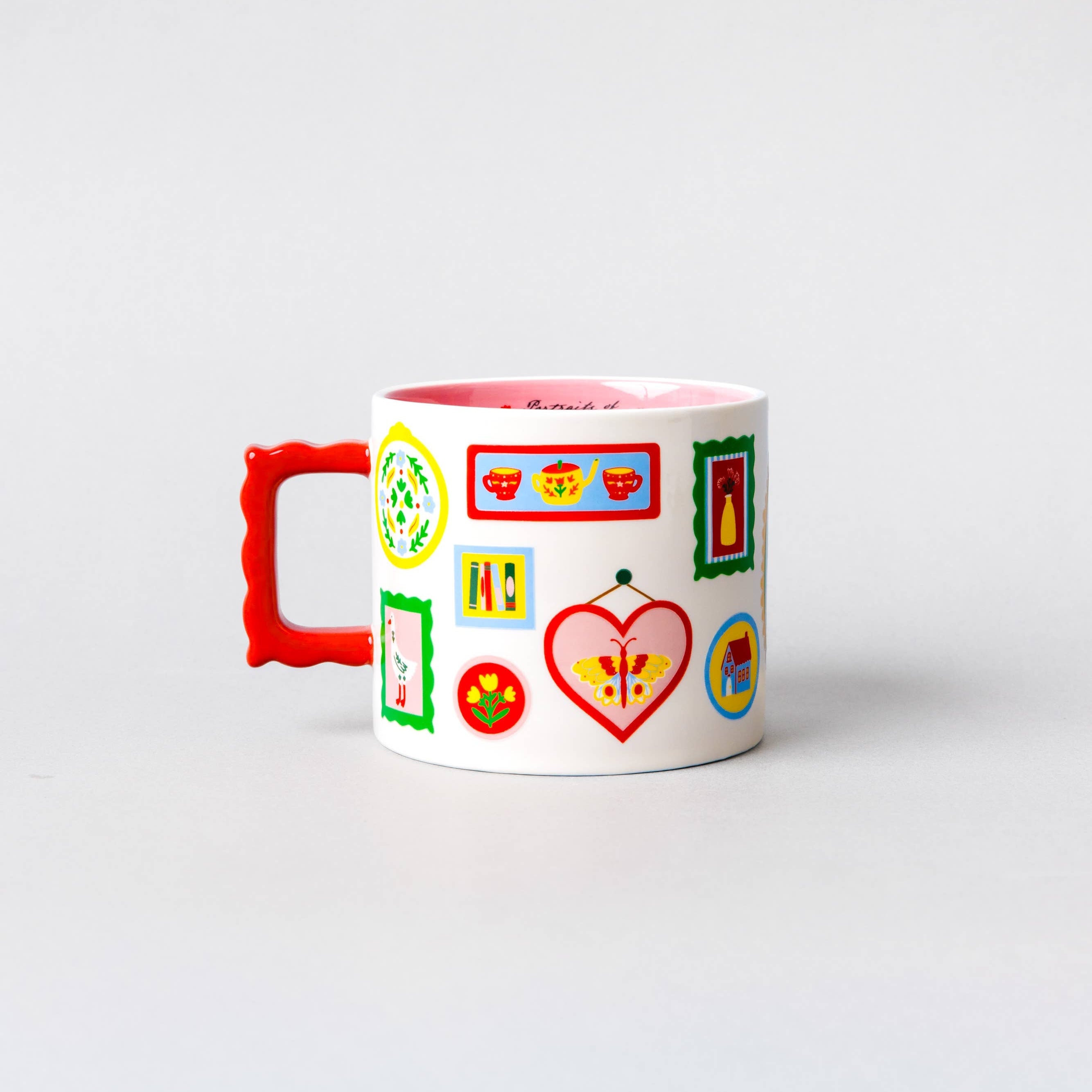A white ceramic mug with a bright red handle and a pink interior, decorated with colorful cartoon-style icons and frames on the side, set against a plain light gray background.