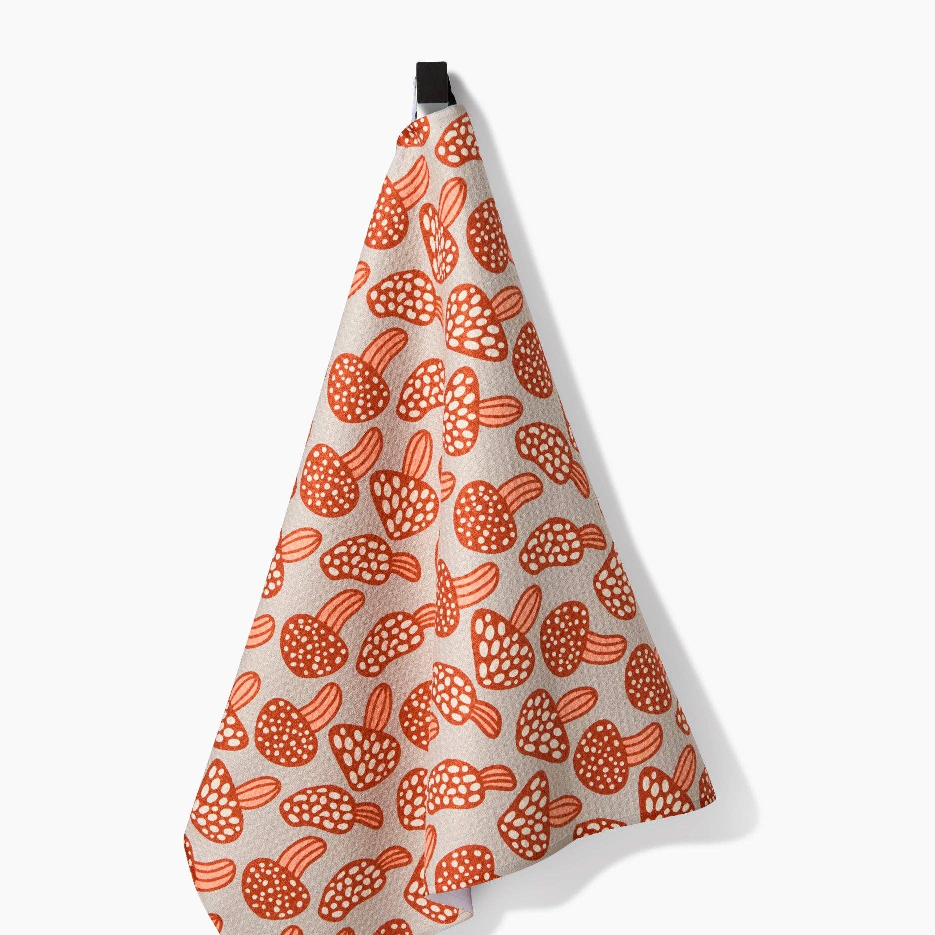 White towel with orange mushroom pattern hanging on a hook against a white background