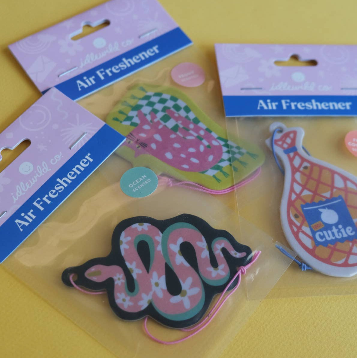 Three air freshener designs on a yellow background