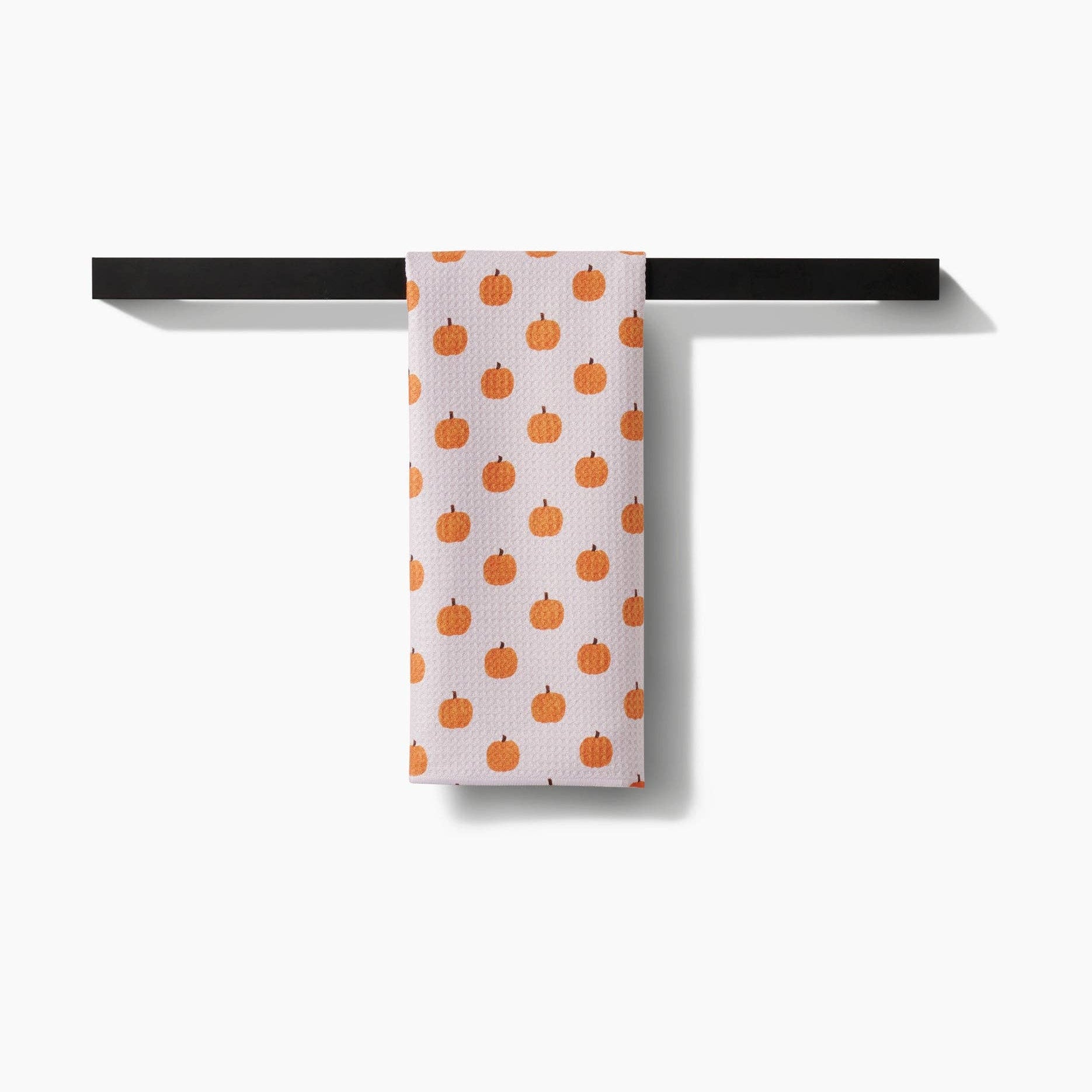 Towel with orange pumpkin pattern hanging on a black rack against a white background