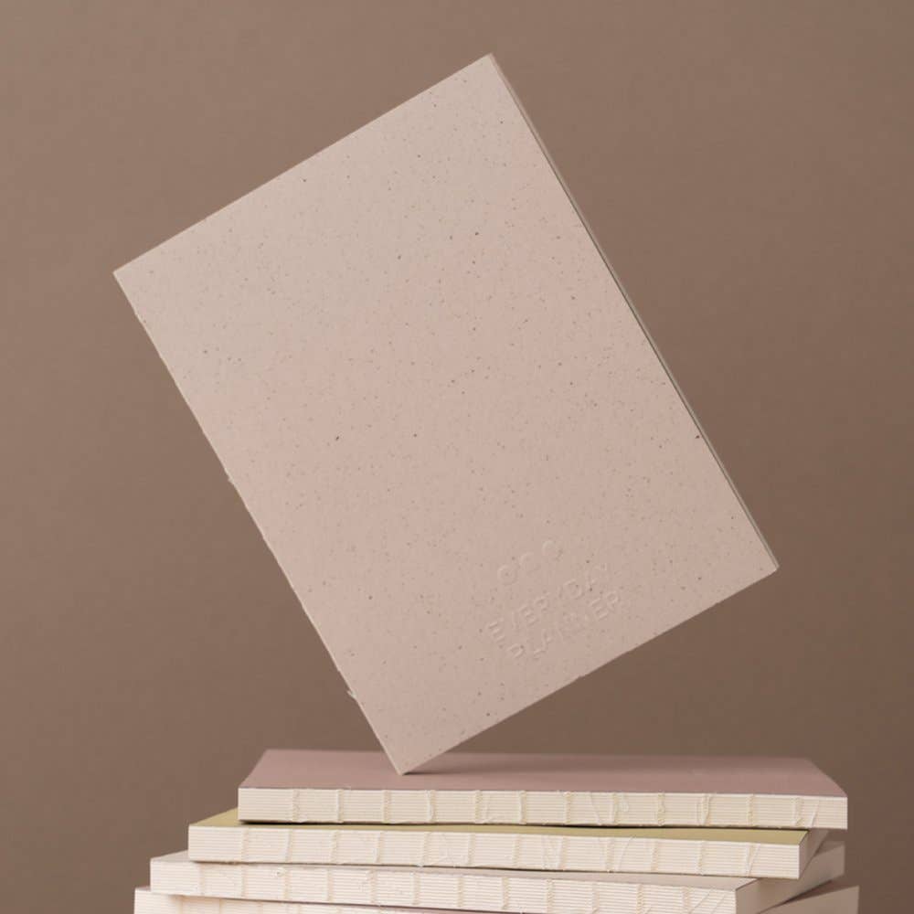 Stack of beige notebooks with one leaning on them against a brown background