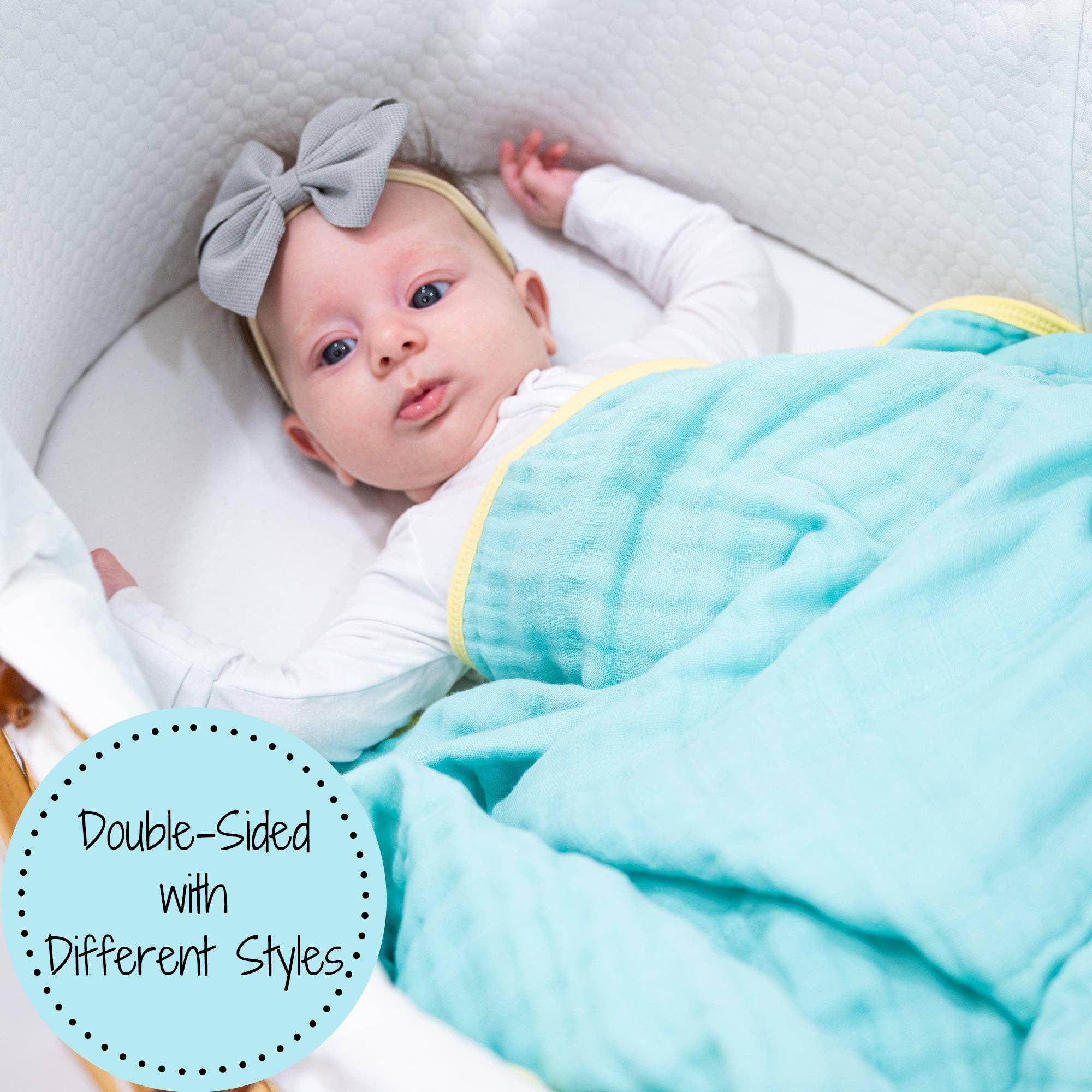 Baby lying on a white blanket with a gray bow, wearing a light blue and yellow double-sided blanket.