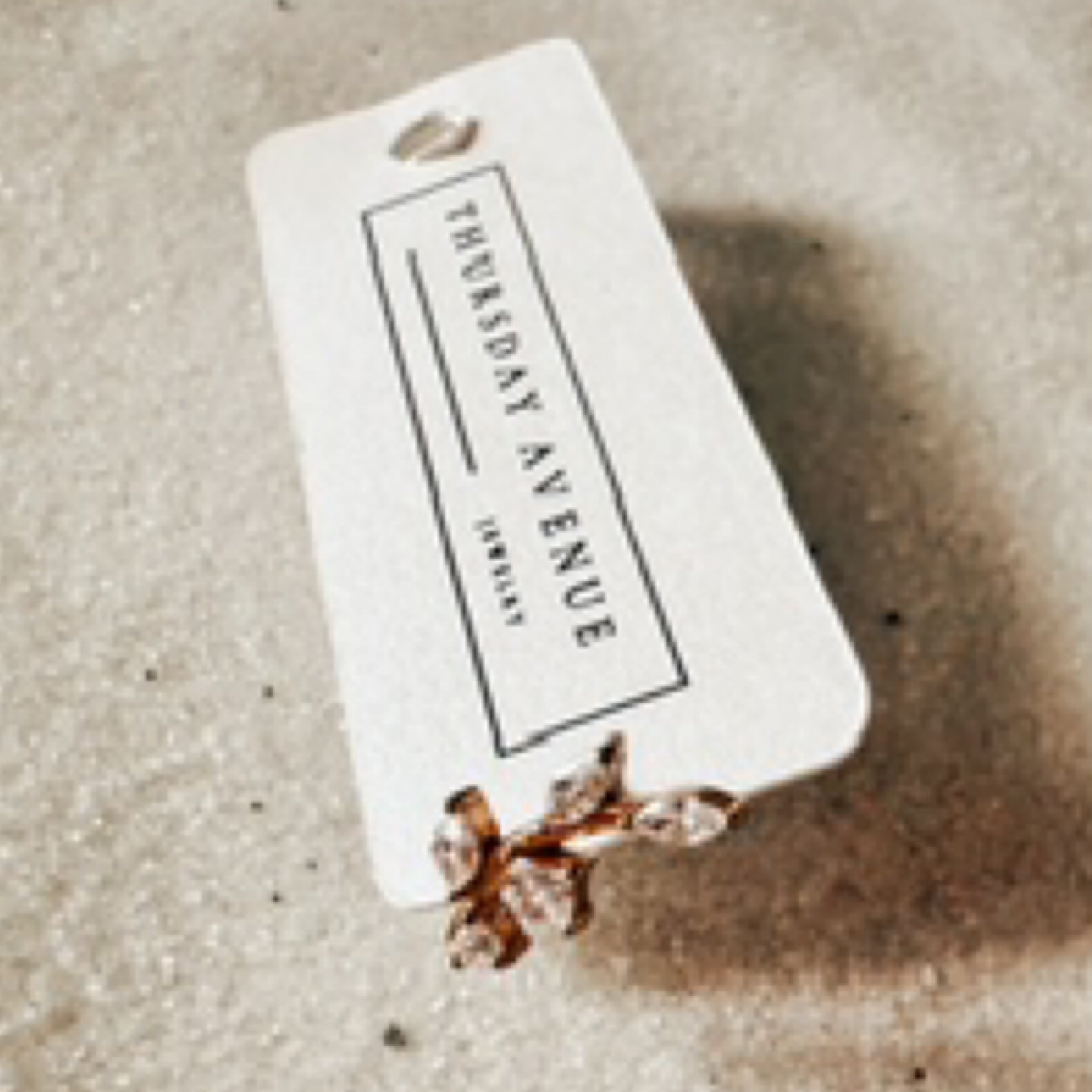 Gold single flat back stud with a tiny diamond branch. Pictured against white sand.