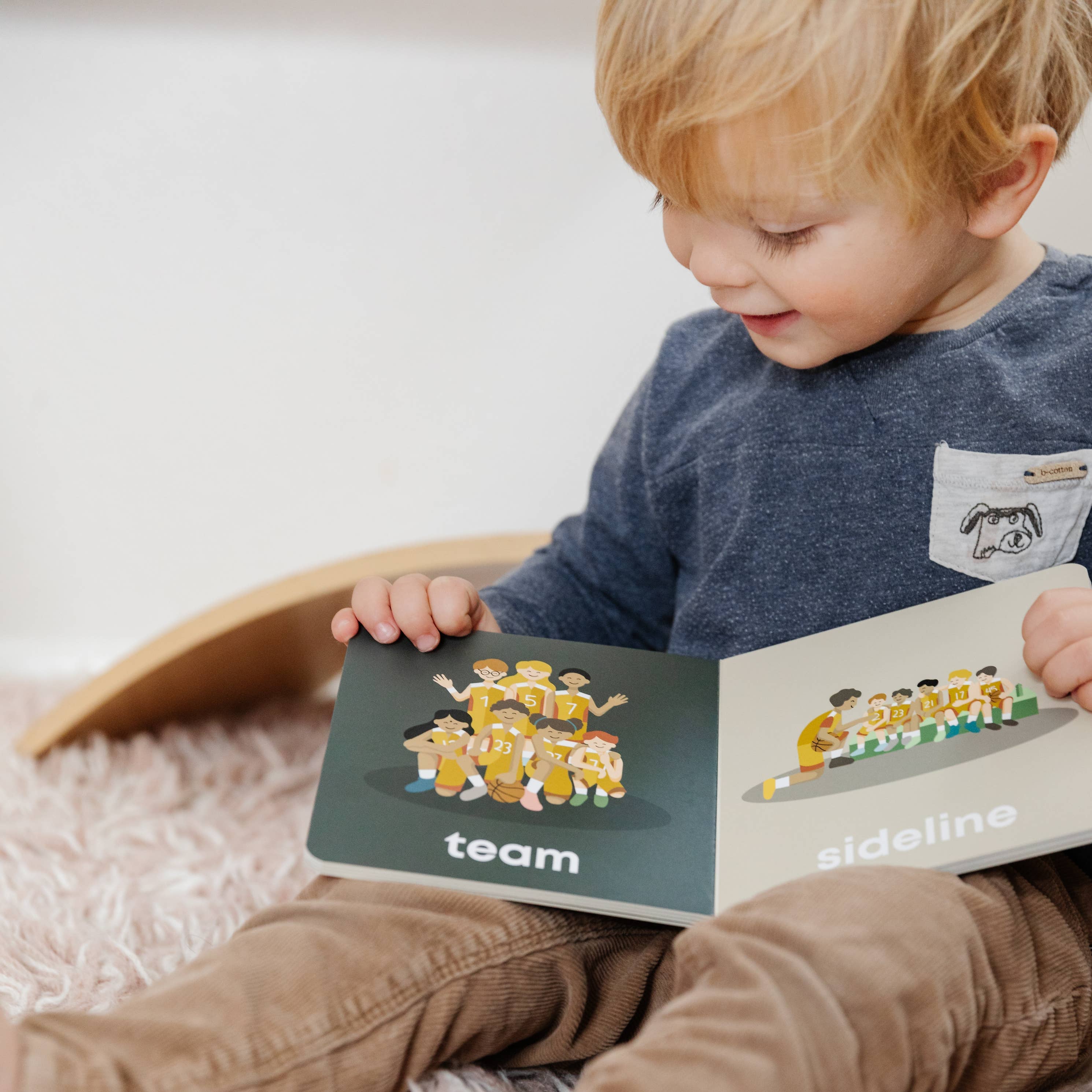 Child reading a book with illustrations of people on a soft surface