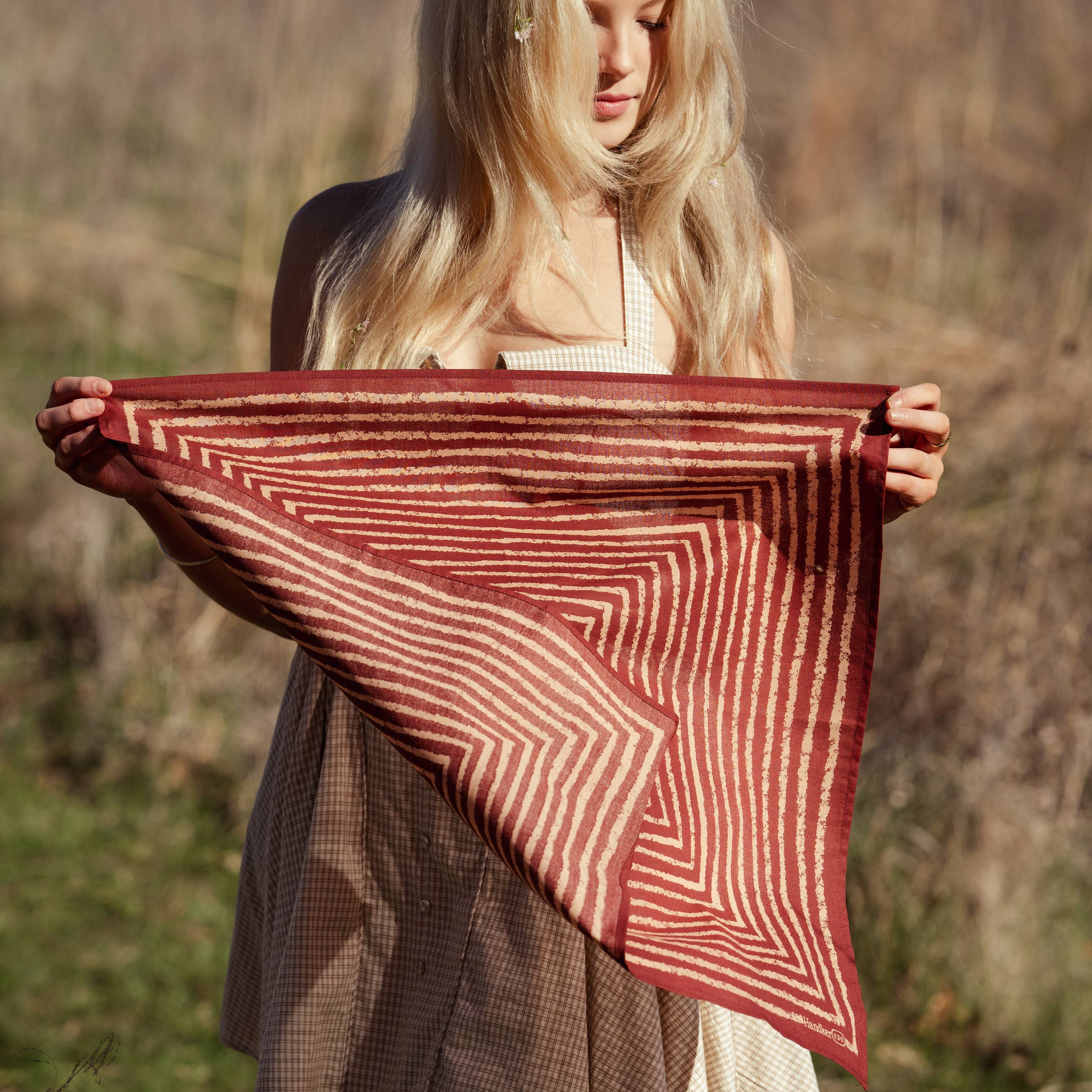 Woman holding a red and white patterned fabric in a natural setting