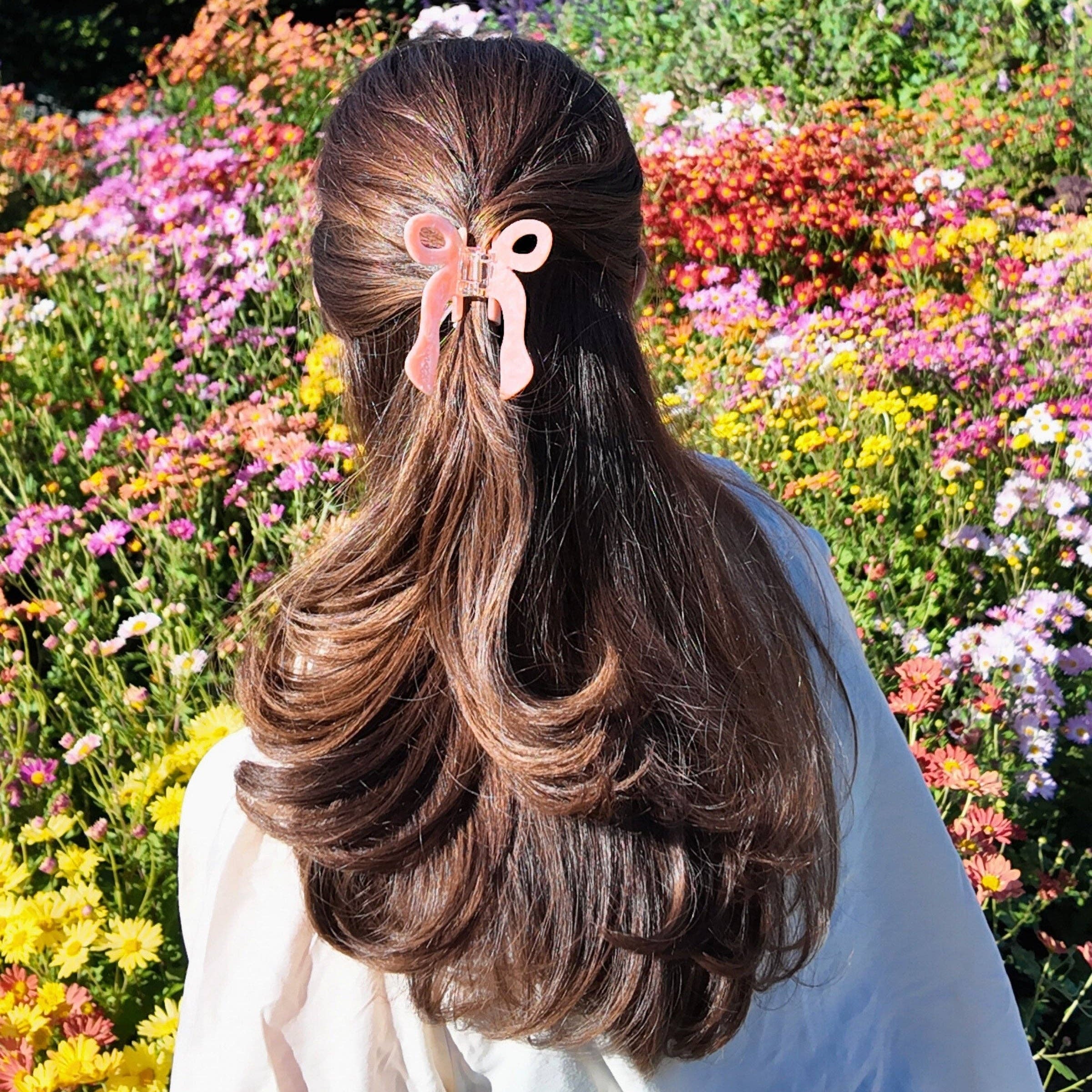 Person with long hair tied back with a pink hair tie standing in a garden of colorful flowers.