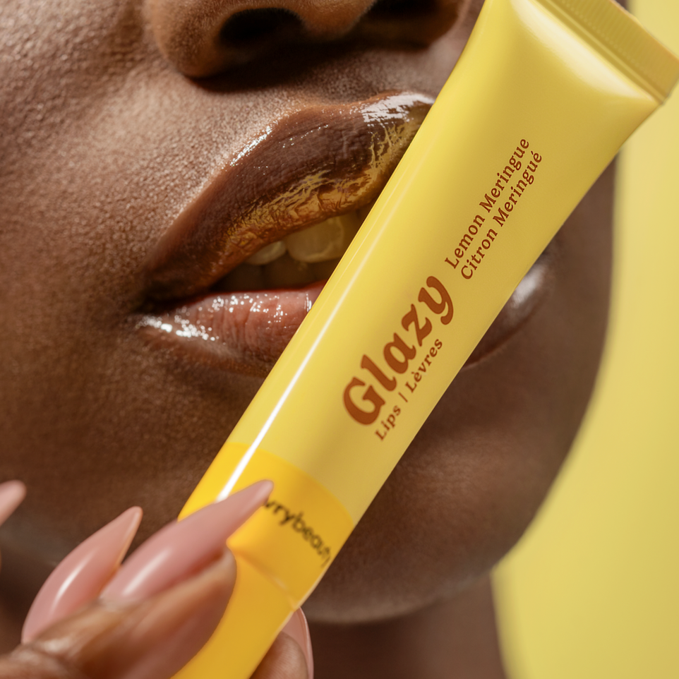 Person holding a yellow Glazy lip balm stick close to their mouth.