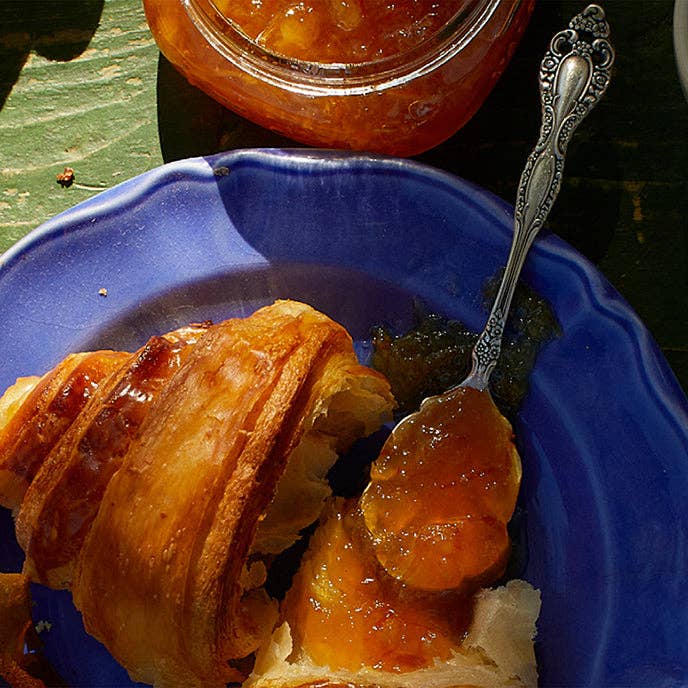 Croissant with orange slices on a blue plate with a silver spoon