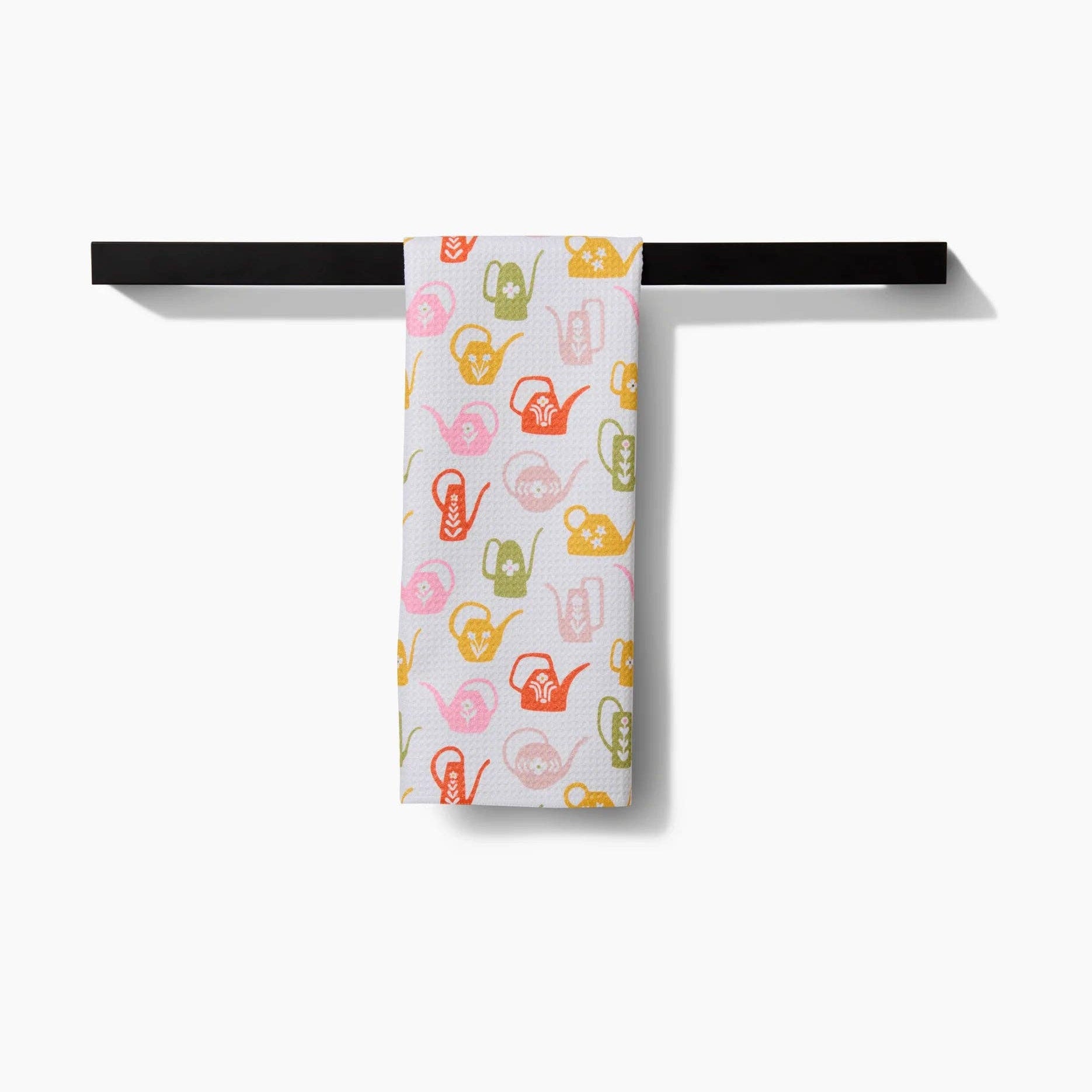 Towel with colorful watering can pattern hanging on a black rack against a white background