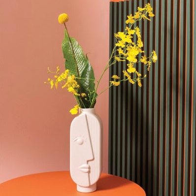 Vase with yellow flowers on an orange surface against a patterned wall.