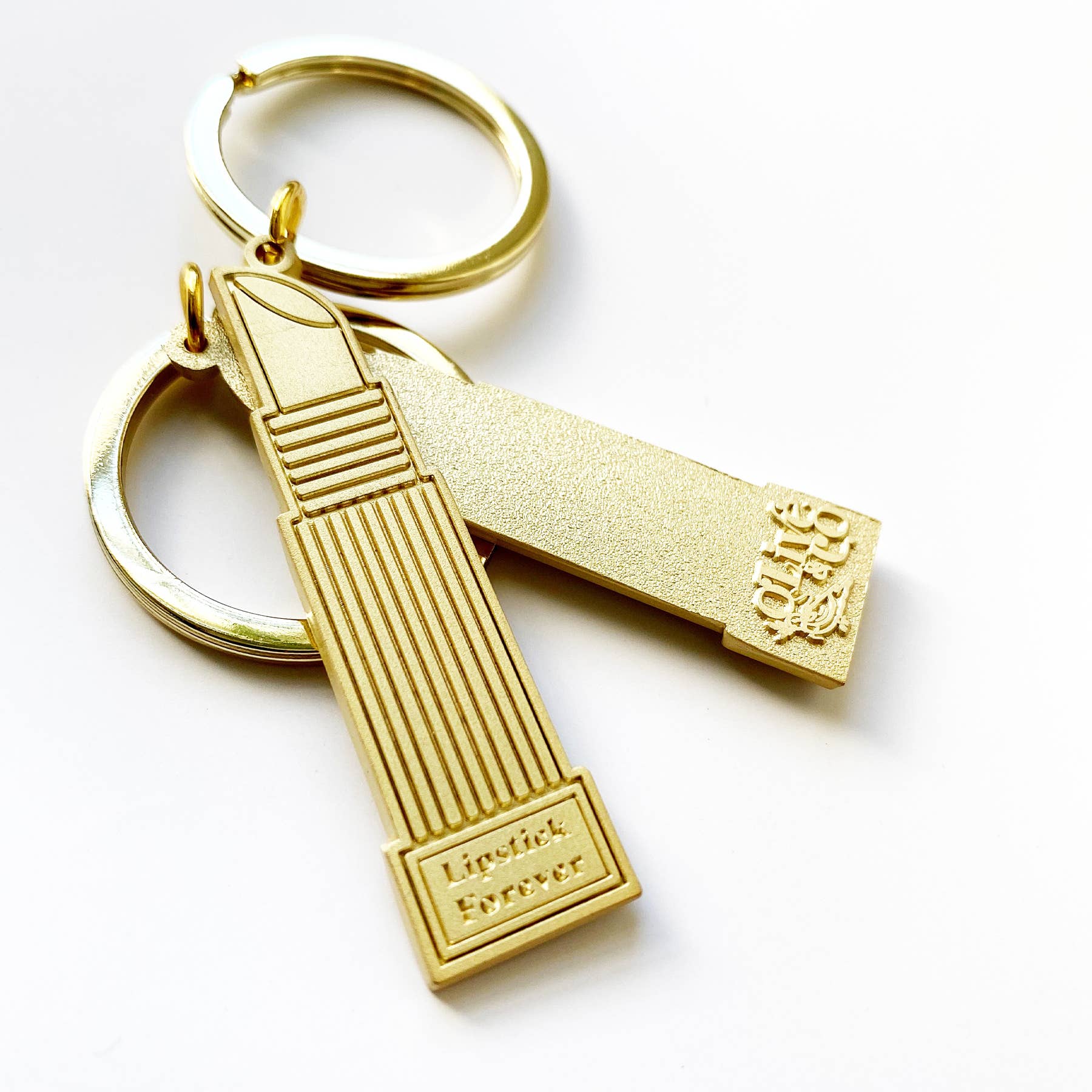 Carry your love of beauty wherever you go with this charming brushed brass keychain. Featuring the empowering "LIPSTICK FOREVER" message on one side and the elegant Olive & Co logo on the back, it's the perfect accessory for makeup enthusiasts and style-conscious individuals alike. Durable and timeless, this keychain celebrates confidence and self-expression in everyday moments.